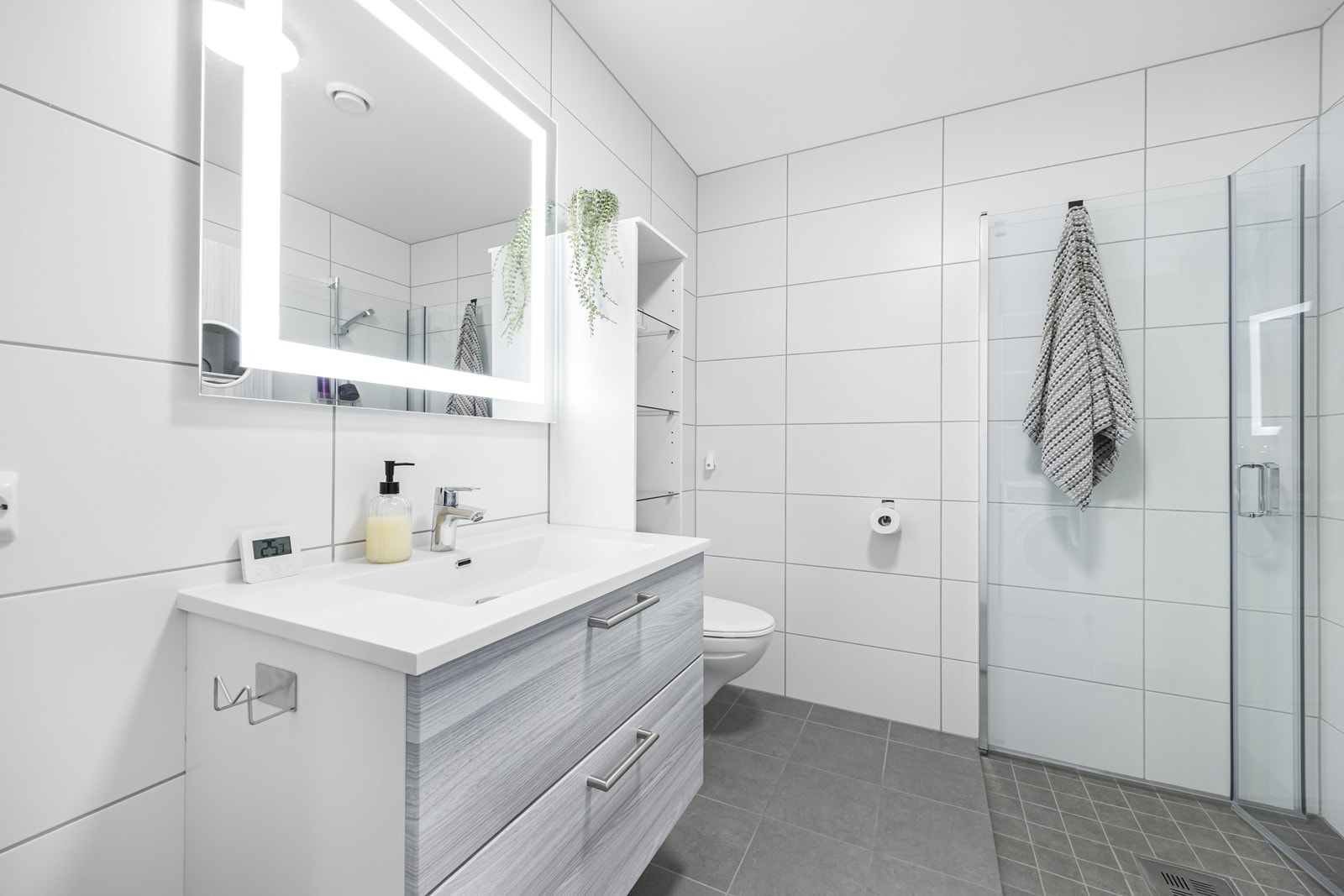 Flislagt bad med varme i gulv. Badet er innredet med dusjnisje med innfellbare dusjdører, vegghengt wc, hvit baderomsinnredning, samt speil med lys i. Galleribilde