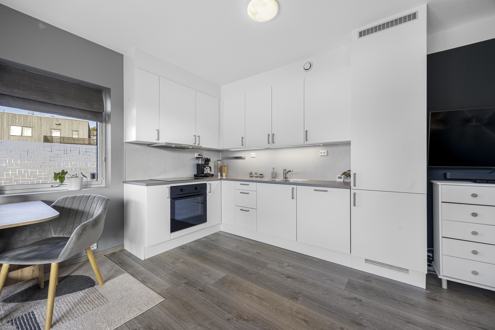 Hvitt, tidløst kjøkken med integrerte hvitevarer, stekeovn, platetopp, kjøl/fryseskap, oppvaskmaskin og ventilator. Galleribilde