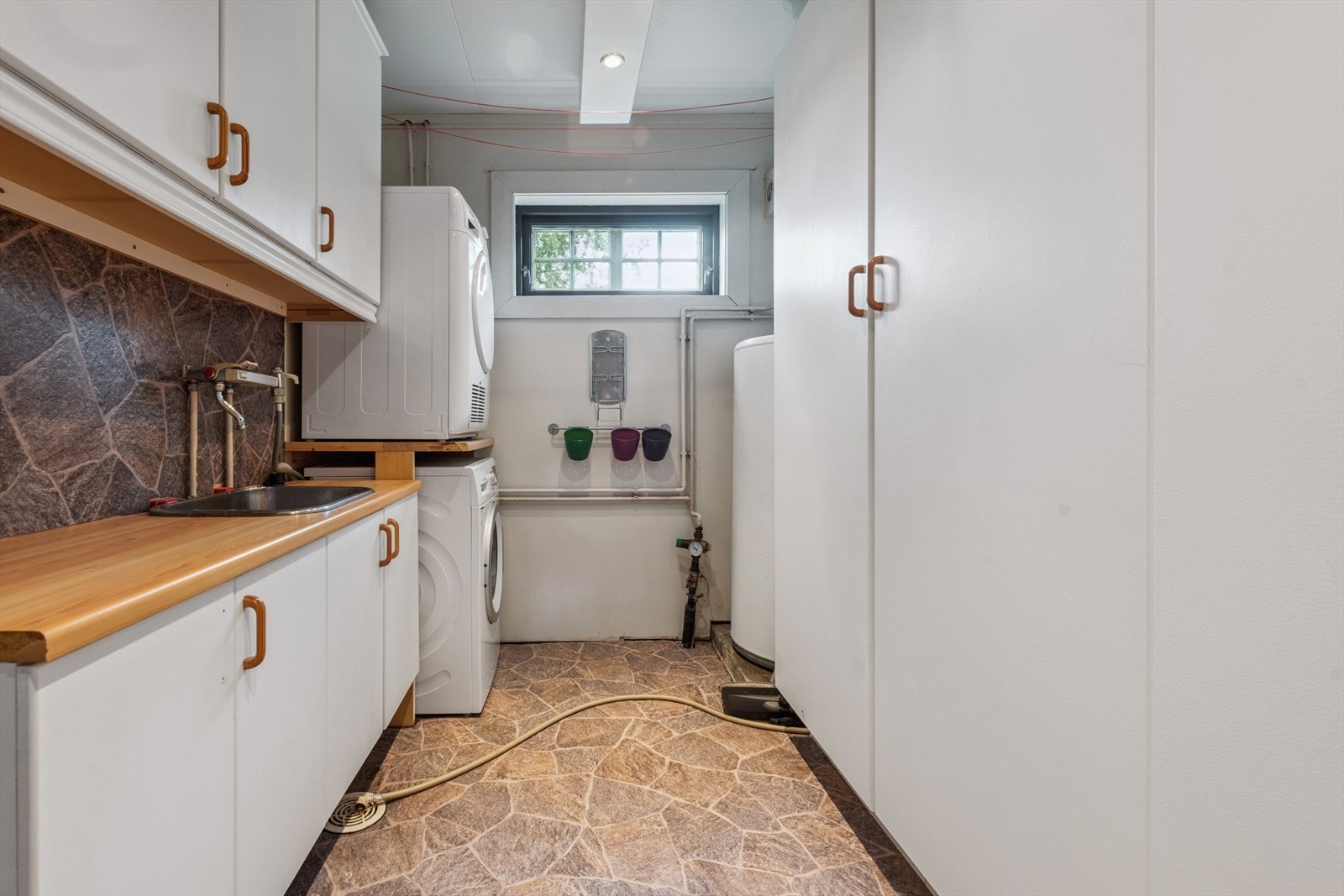 Praktisk vaskerom med opplegg for vaskemaskin og tørketrommel. Her er det god plass til lagring av utstyr i garderobeskap, over og underskap. Galleribilde