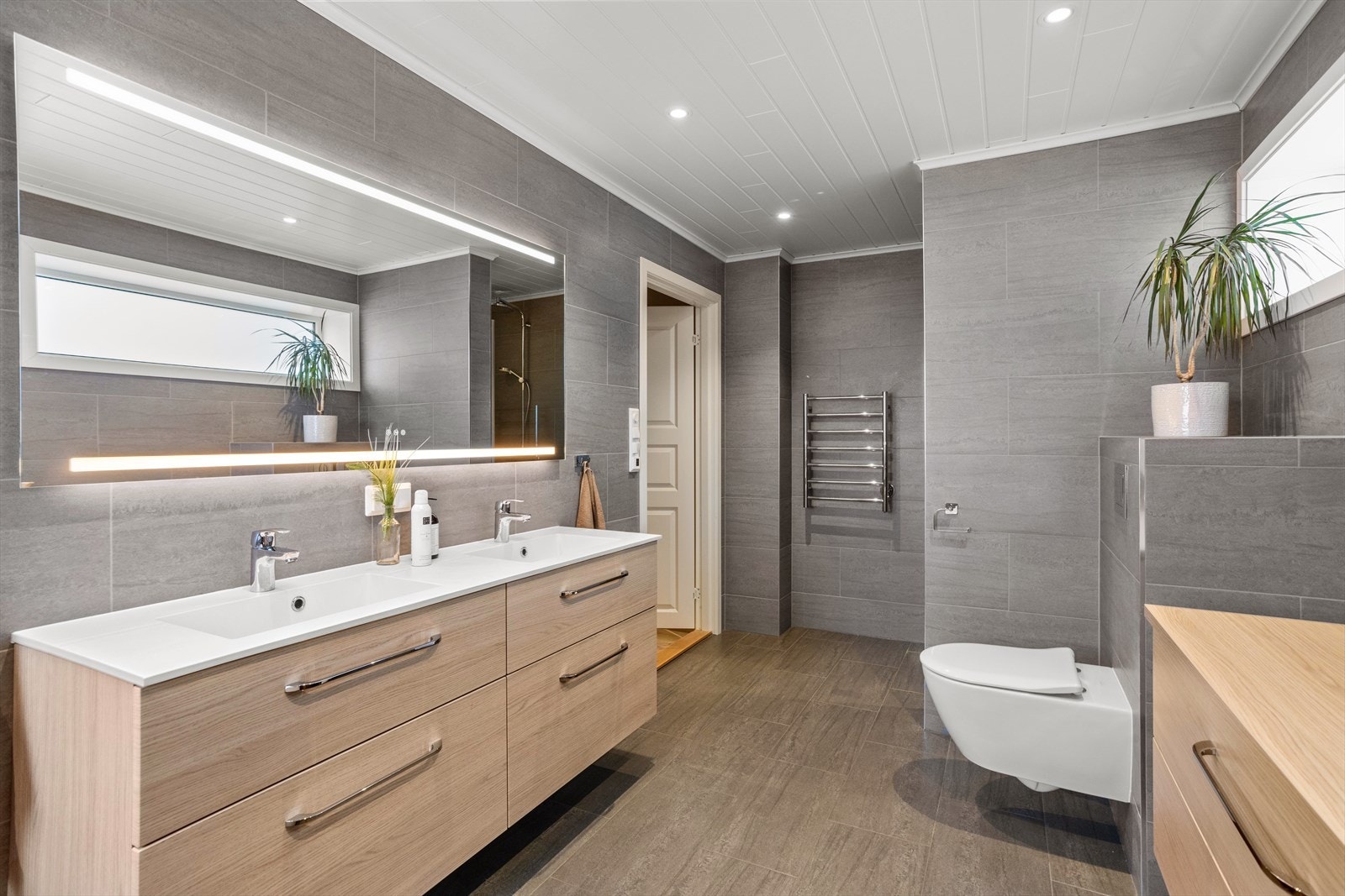 Videre har badet doble servanter, speil i hele benkens bredde med integrert belysning, samt veggmontert wc. Galleribilde