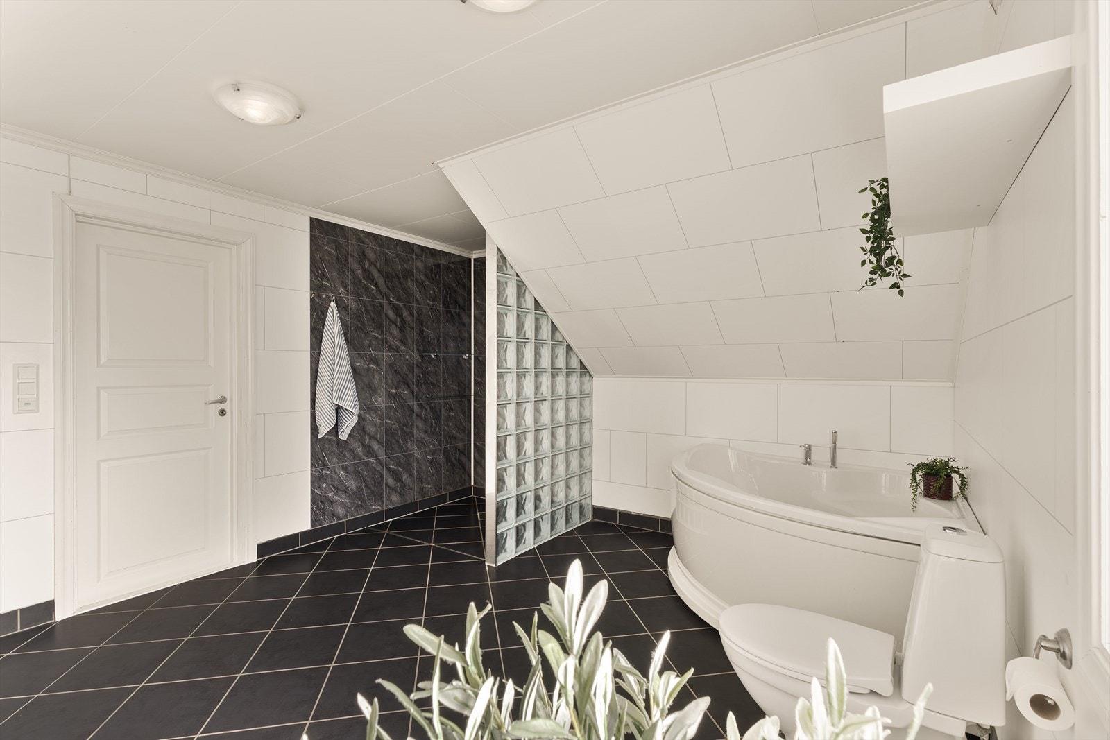 Badet er innredet med toalett, dusj med glassbyggersteinsvegg, hjørnebadekar, veggskap samt dobbel servant med speil og belysning Galleribilde