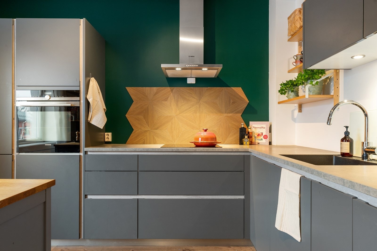 En grønn kontrastvegg kombinert med backsplash i tre gir kjøkkenet et særpreget og moderne uttrykk. Galleribilde