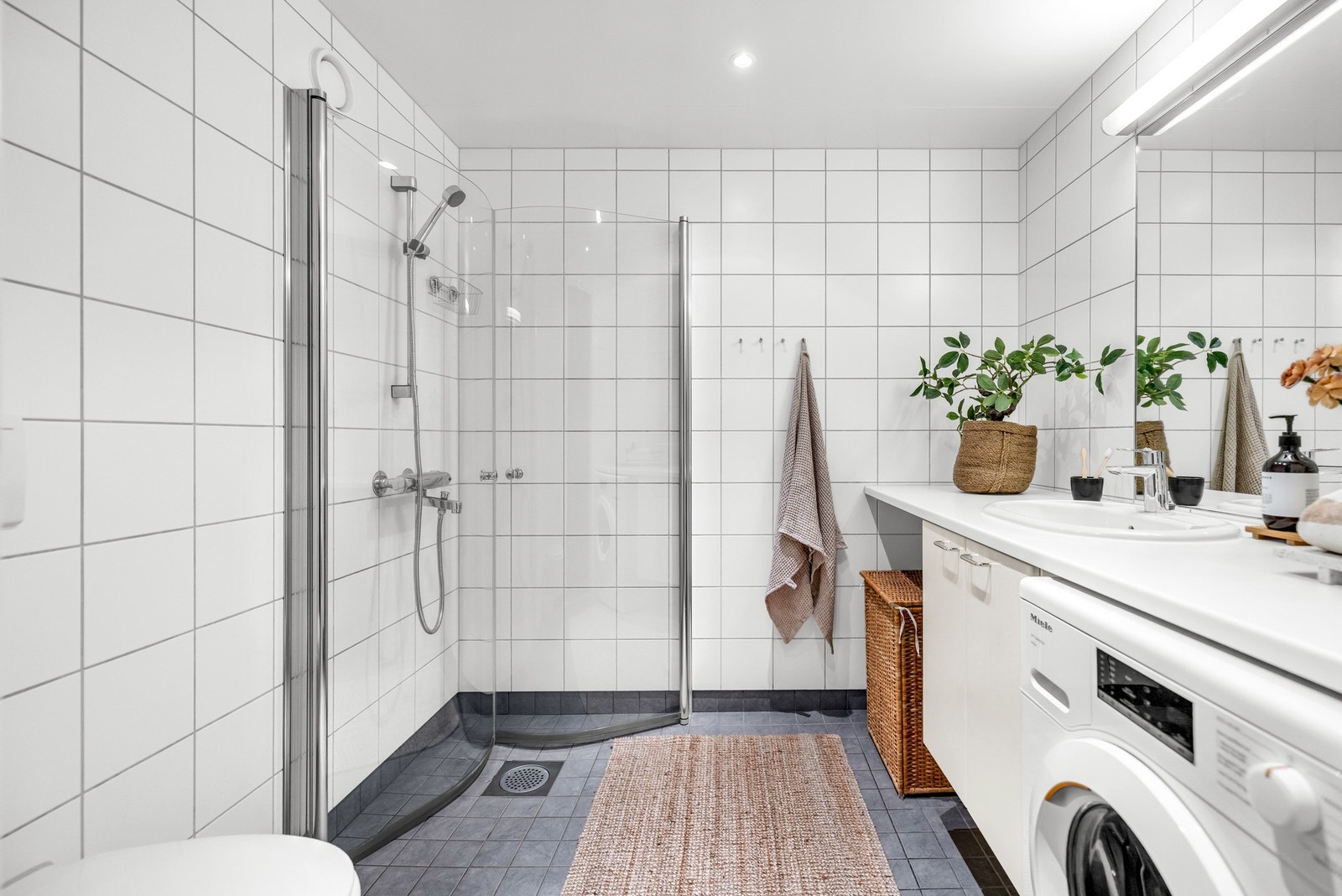 Badet er innredet med dusjhjørne med innfellbare glassvegger, servantseksjon med underskap og vegghengt toalett, samt opplegg for vaskemaskin Galleribilde