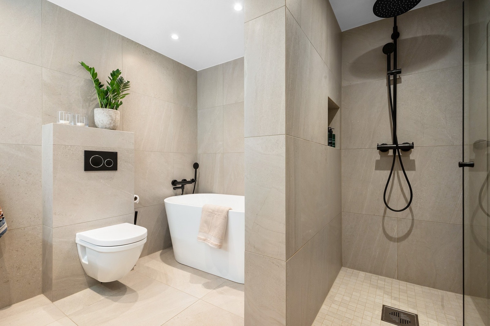 Rommet har store, rektangulære fliser i en tidsriktig beigefarge og delikat baderomsinnredning Galleribilde