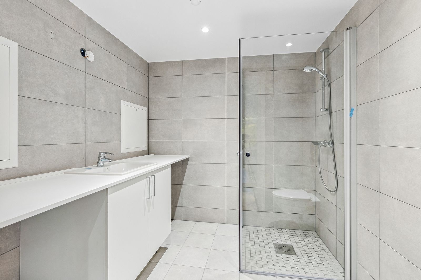 Pent bad med lyse fliser, smart oppbevaring og dusjhjørne med innfellbare glassdører som utnytter plassen effektivt. Videre har badet et vegghengt toalett og opplegg for vaskemaskin. Galleribilde