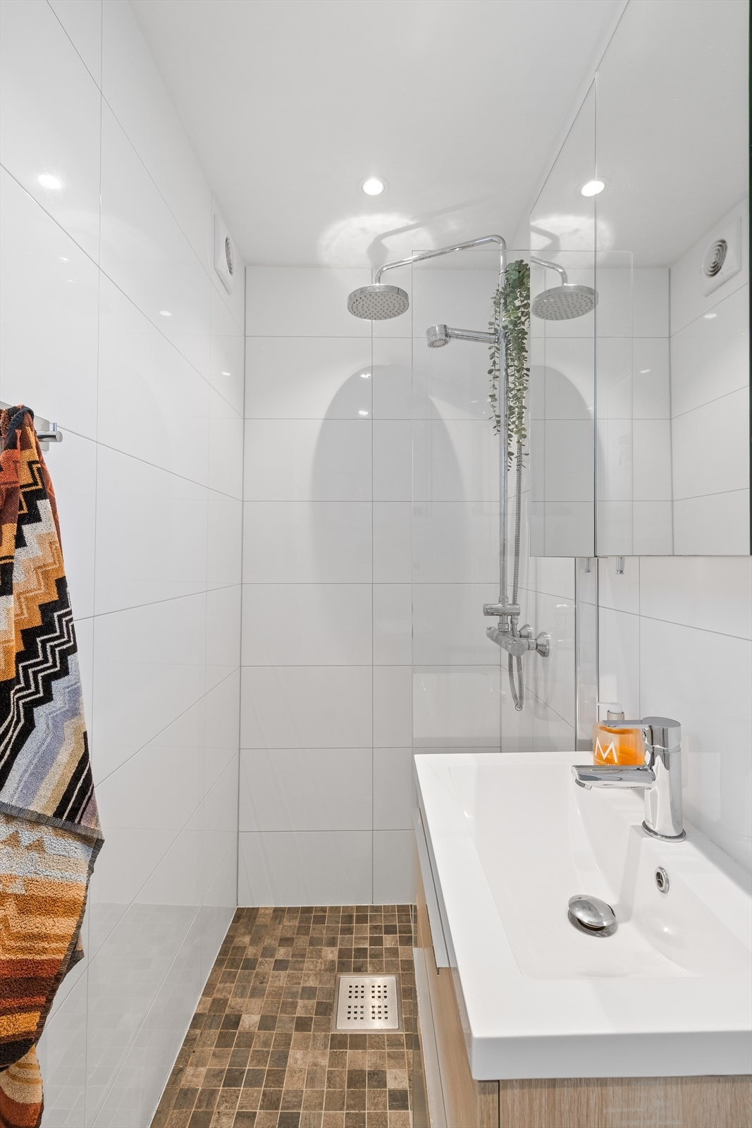 Badet er innredet med nedfelt servant, veggmontert toalett og dusjvegger/hjørne. Det er elektriske varmekabler på gulv Galleribilde