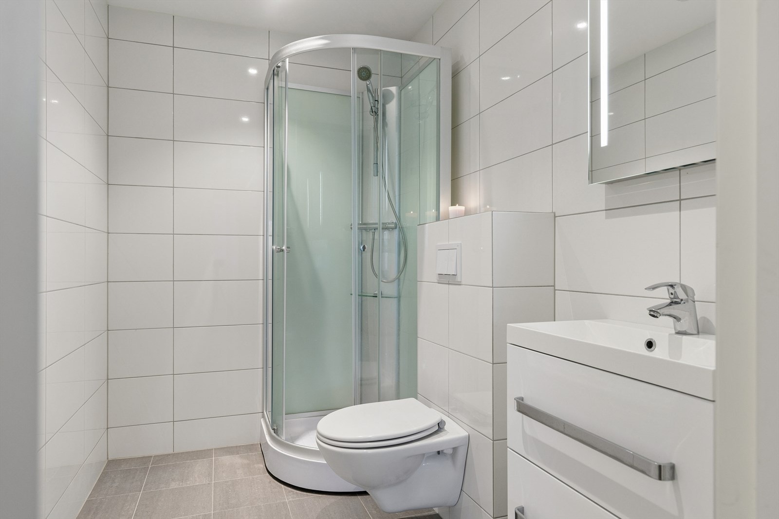 Pent helfliset bad. Rommet har dusjkabinett, seksjon med vask og veggmontert toalett. Galleribilde