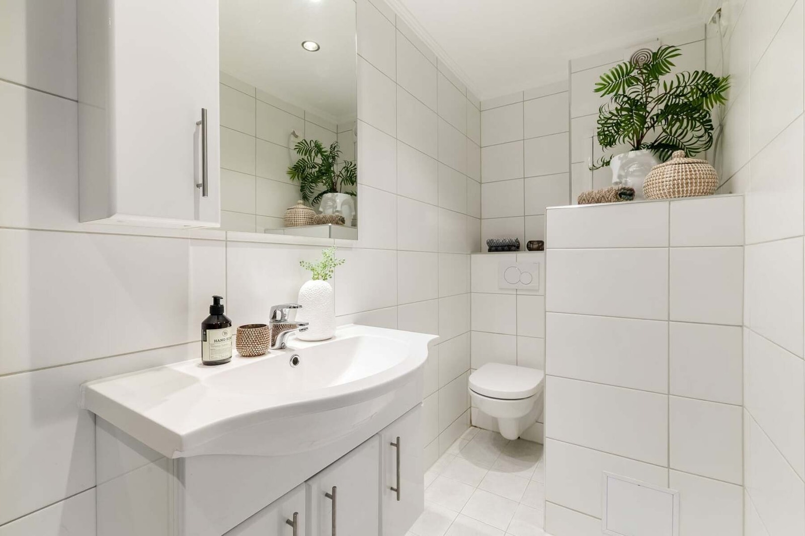 Badet er utstyrt med dusjhjørne, servant med innredning, vegghengt toalett og opplegg for vaskemaskin. Varmtvannsberederen er diskret plassert i en lukket, flislagt kasse. Galleribilde