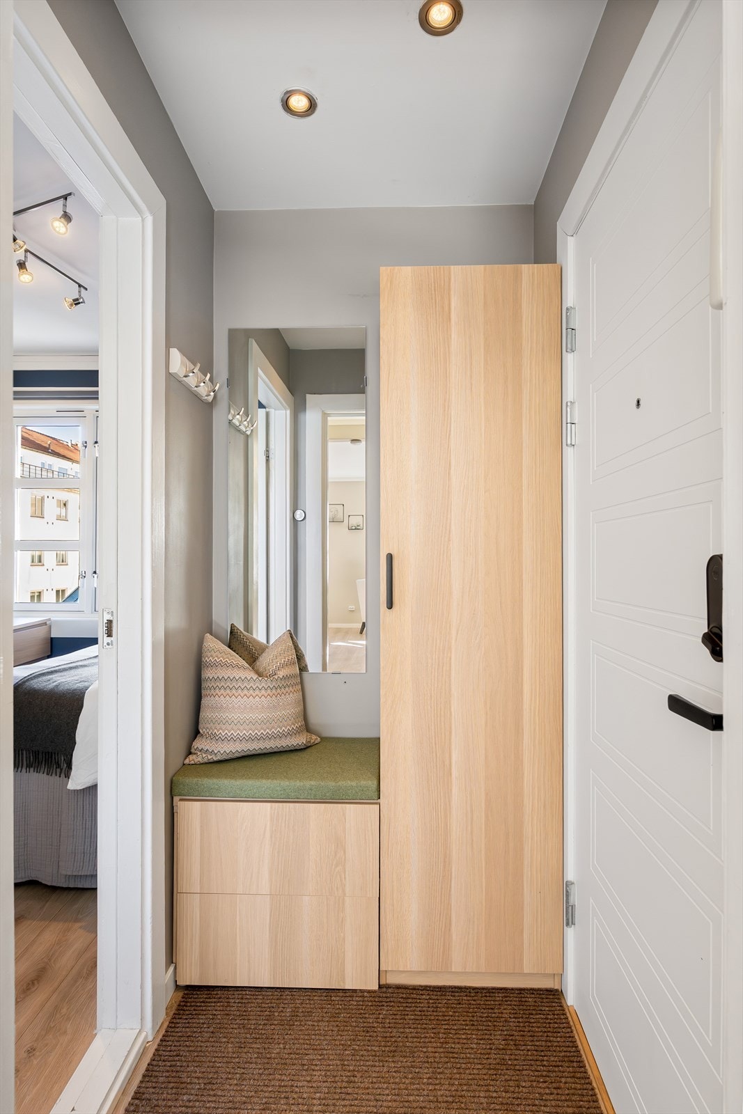 Her møtes du av en spesialtilpasset garderobeløsning basert på BESTÅ og PAX fra IKEA, med god oppbevaringsplass. Vegghengt speil og ekstra knagger er montert for praktisk oppbevaring. Galleribilde