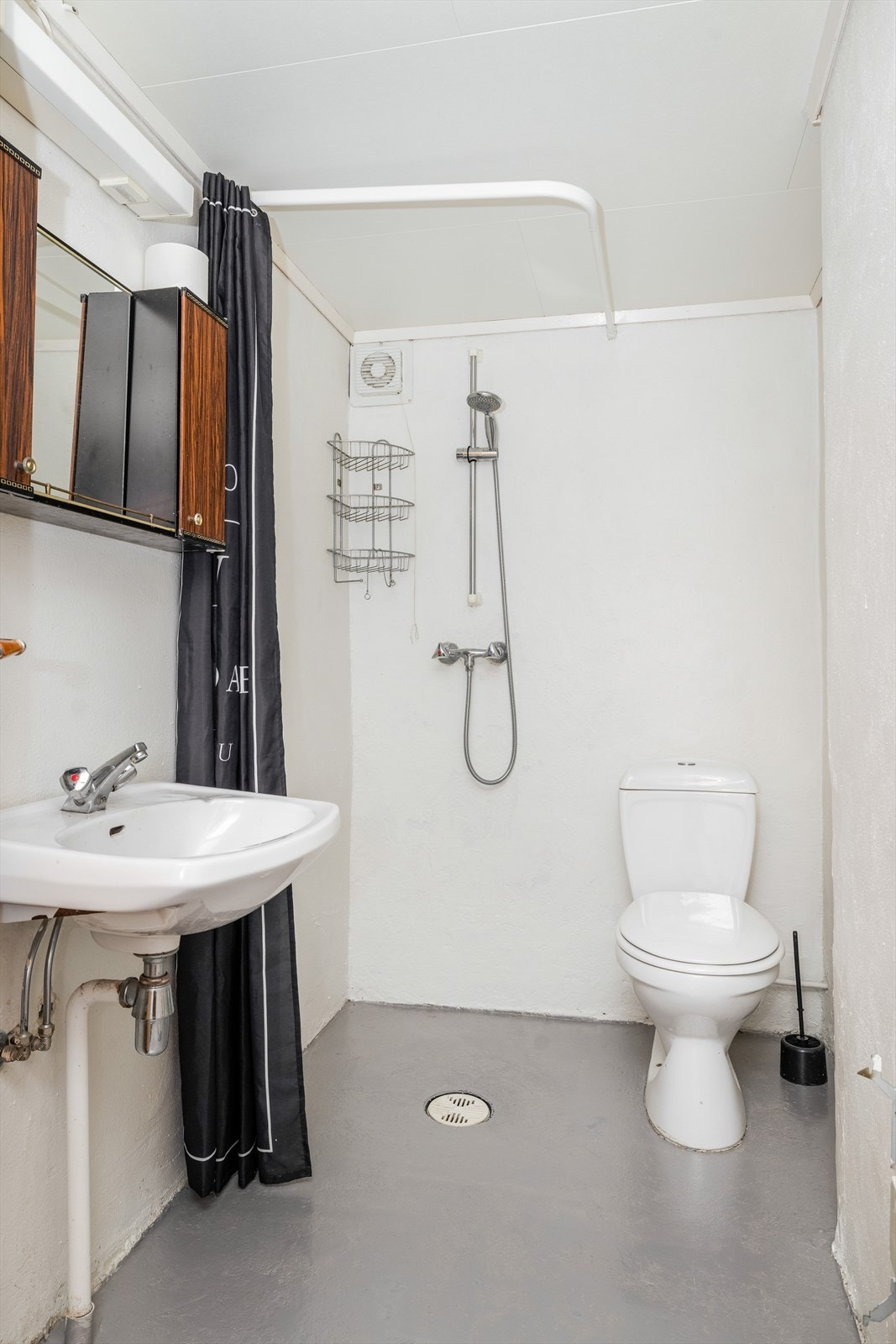 Badet i underetasjen er av eldre standard, utstyrt med toalett, vegghengt servant og dusjhjørne med forheng. Galleribilde