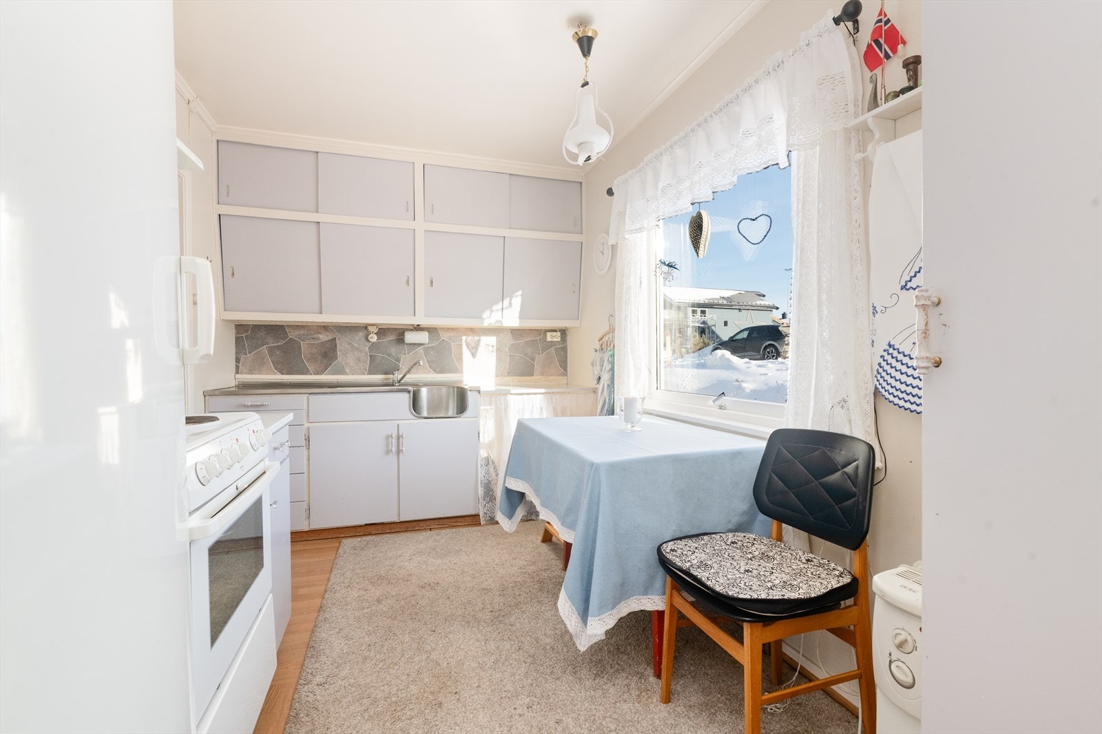 Lyst og romslig kjøkken med takhøy kjøkkeninnredning av eldre dato og fin plass til kjøkkenbord i forbindelse med vindu. Galleribilde