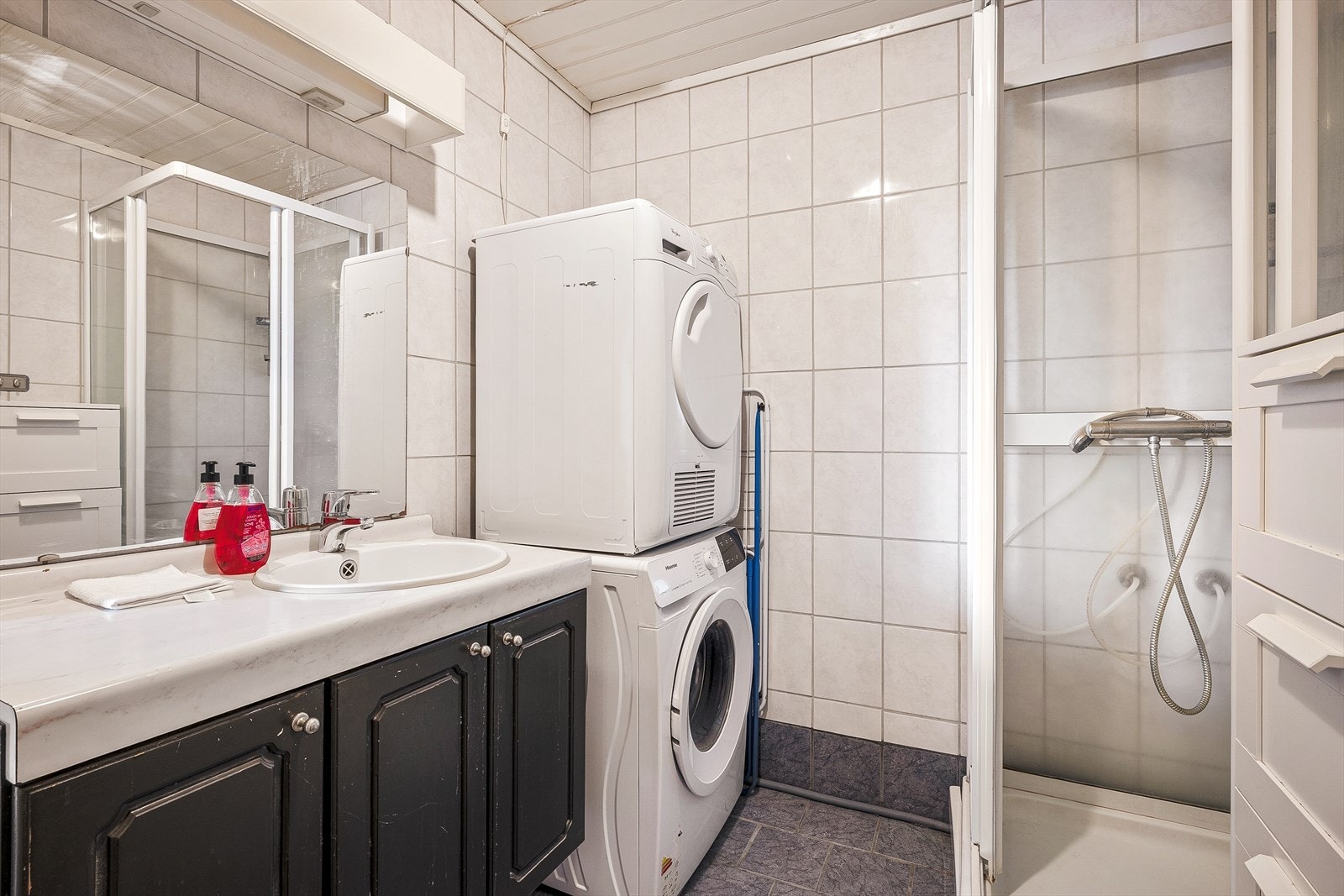 Badet er innredet med servant i møbel, speil, skap, toalett, dusjkabinett og opplegg for vaskemaskin. Galleribilde