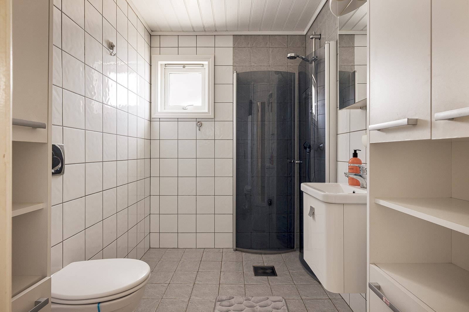 Badet er innredet med servant i møbel, speilskap, vegghengt toalett og dusj med glassdører. Galleribilde