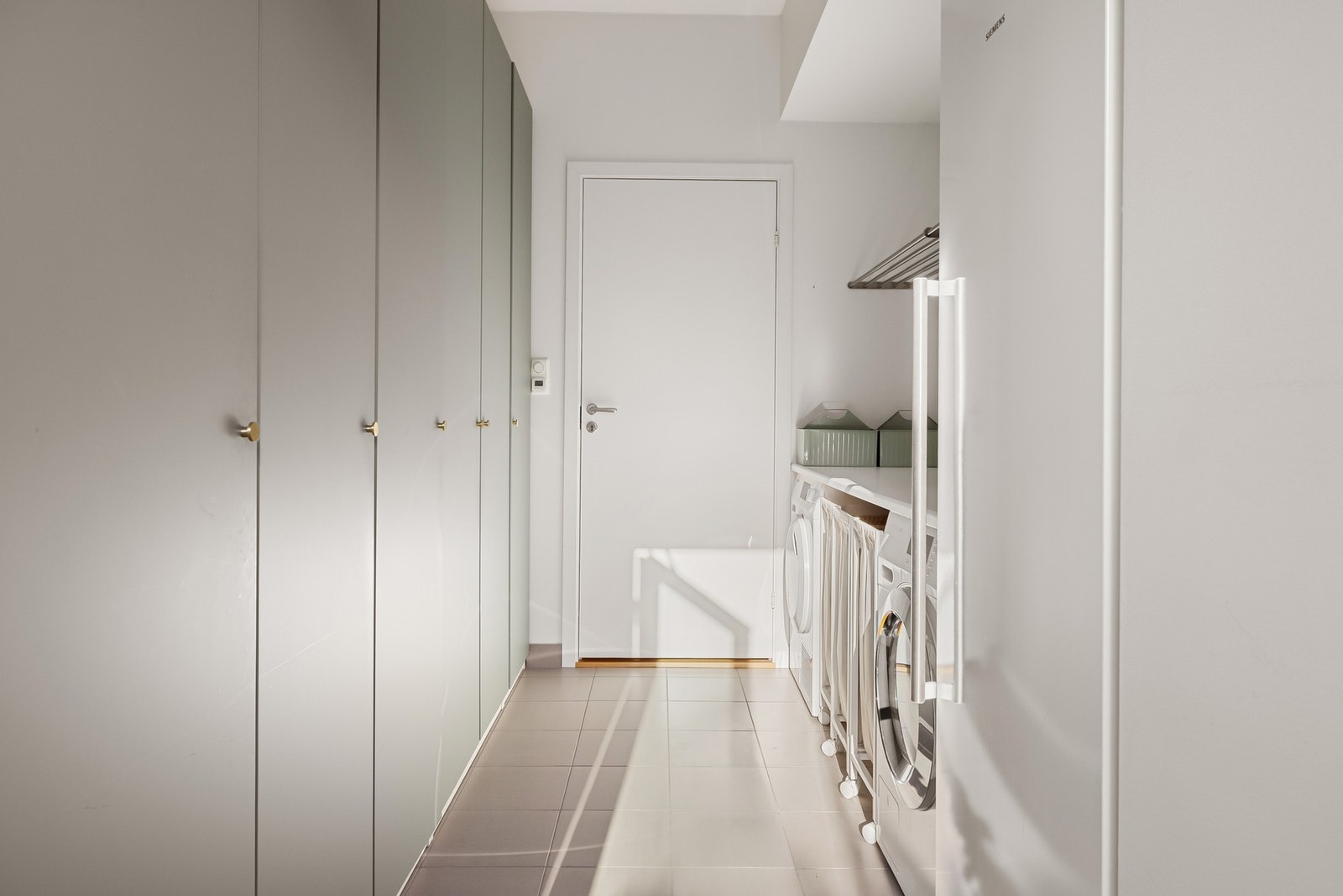 På ene siden er det satt inn store garderobeskap for oppbevaring, og på andre siden er det en benkeplate med opplegg for vaskemaskin og plass til tørketrommel under. Galleribilde