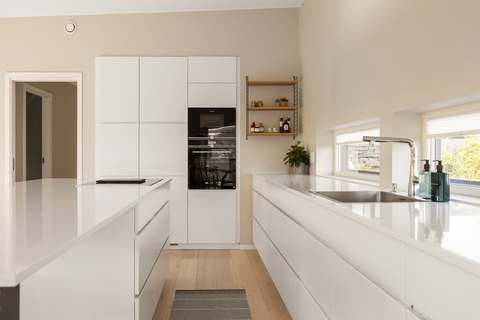 Kjøkkeninnredningen består av hvite slette fronter med integrerte håndtak og en benkeplate i Iconic hvit Silestone. Galleribilde