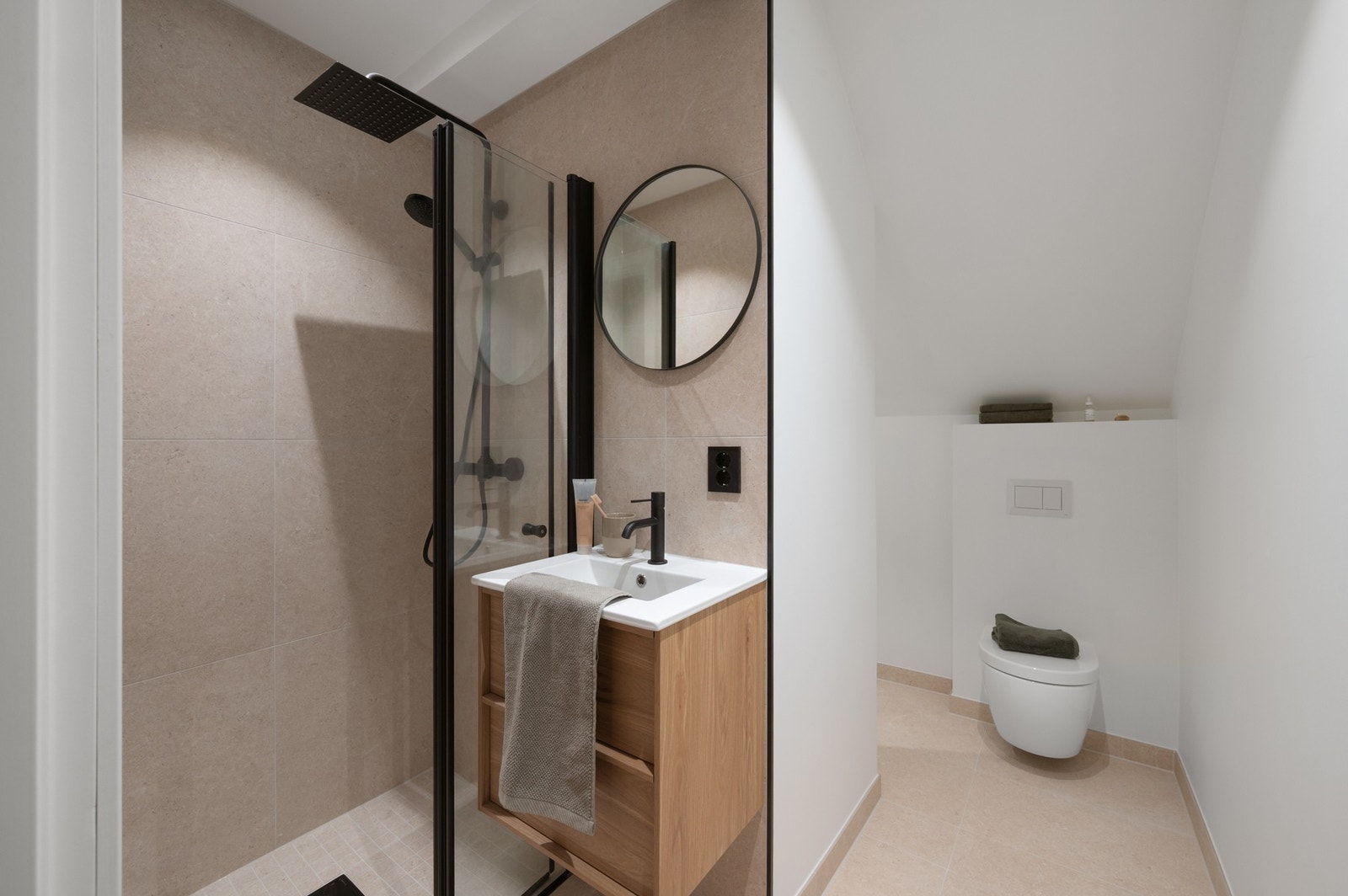 Badet inneholder vegghengt toalett, helstøpt servant, skuffer under servant med slette fronter, dusjdører i klart glass og opplegg for vaskemaskin. Galleribilde