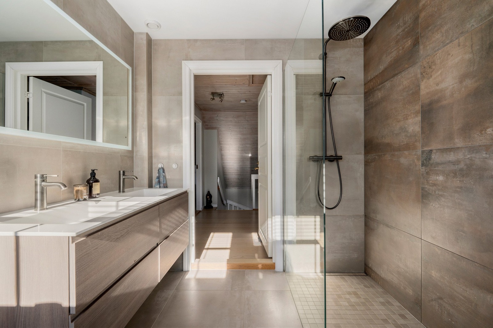 Badet har speil med integrert belysning over servant, vegghengt toalett og dusjhjørne med glassvegg Galleribilde