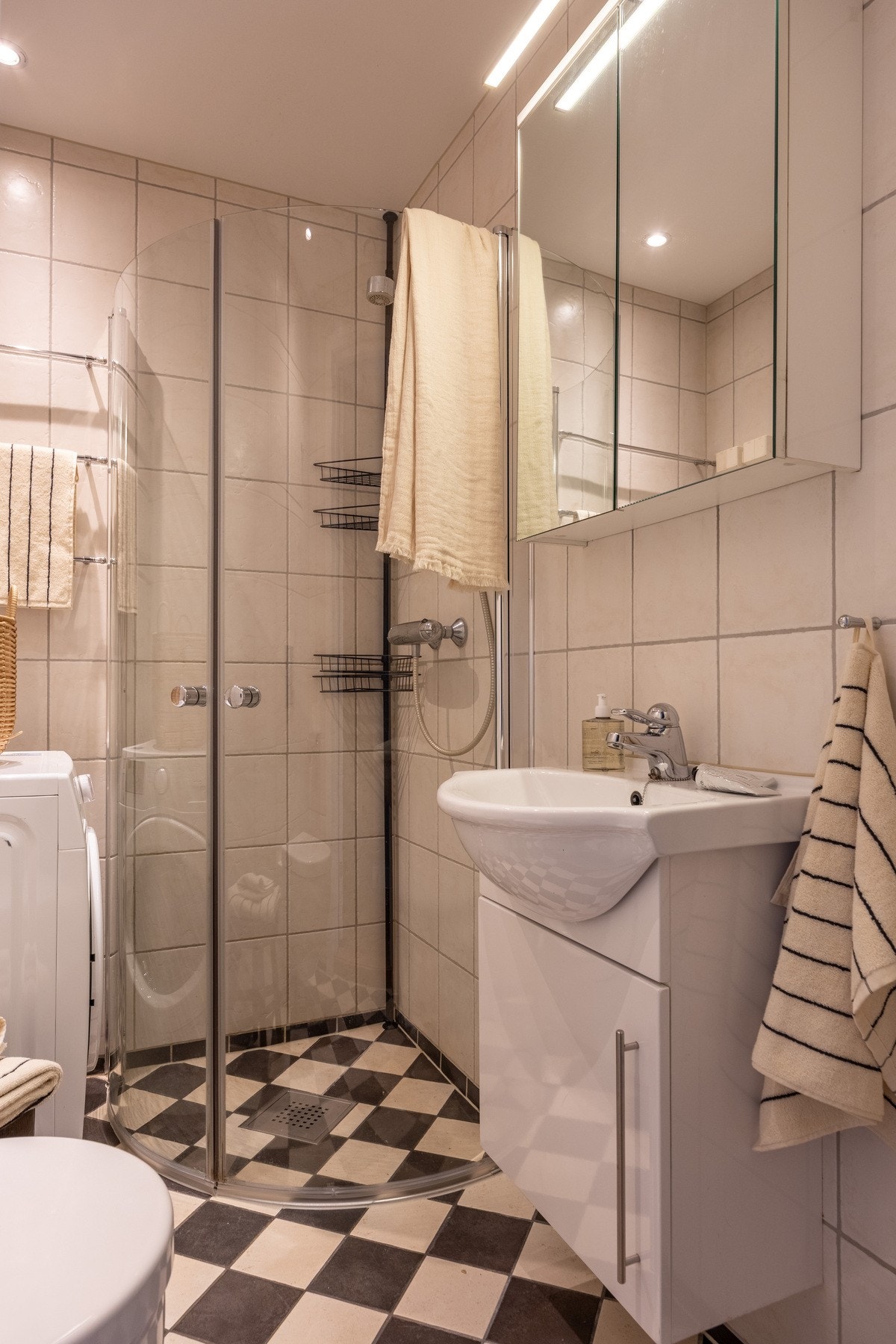 Dusjhjørne med innfellbare buede glassdører, innredning med underskap med heldekkende servant og overskap med speil. Galleribilde