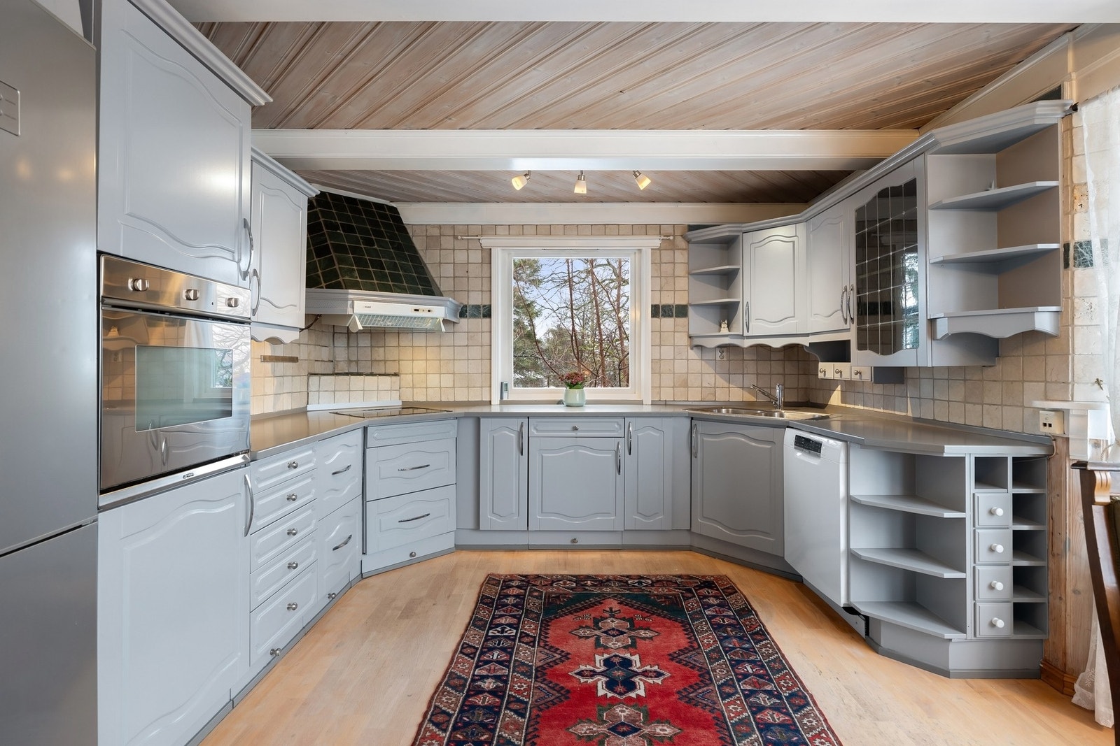 Hjørneløsning med nedfelt platetopp og flislagt ventilatorhette med avtrekk ut. Oppvaskmaskin og kjøl- fryseskap og integrert stekeovn. Galleribilde