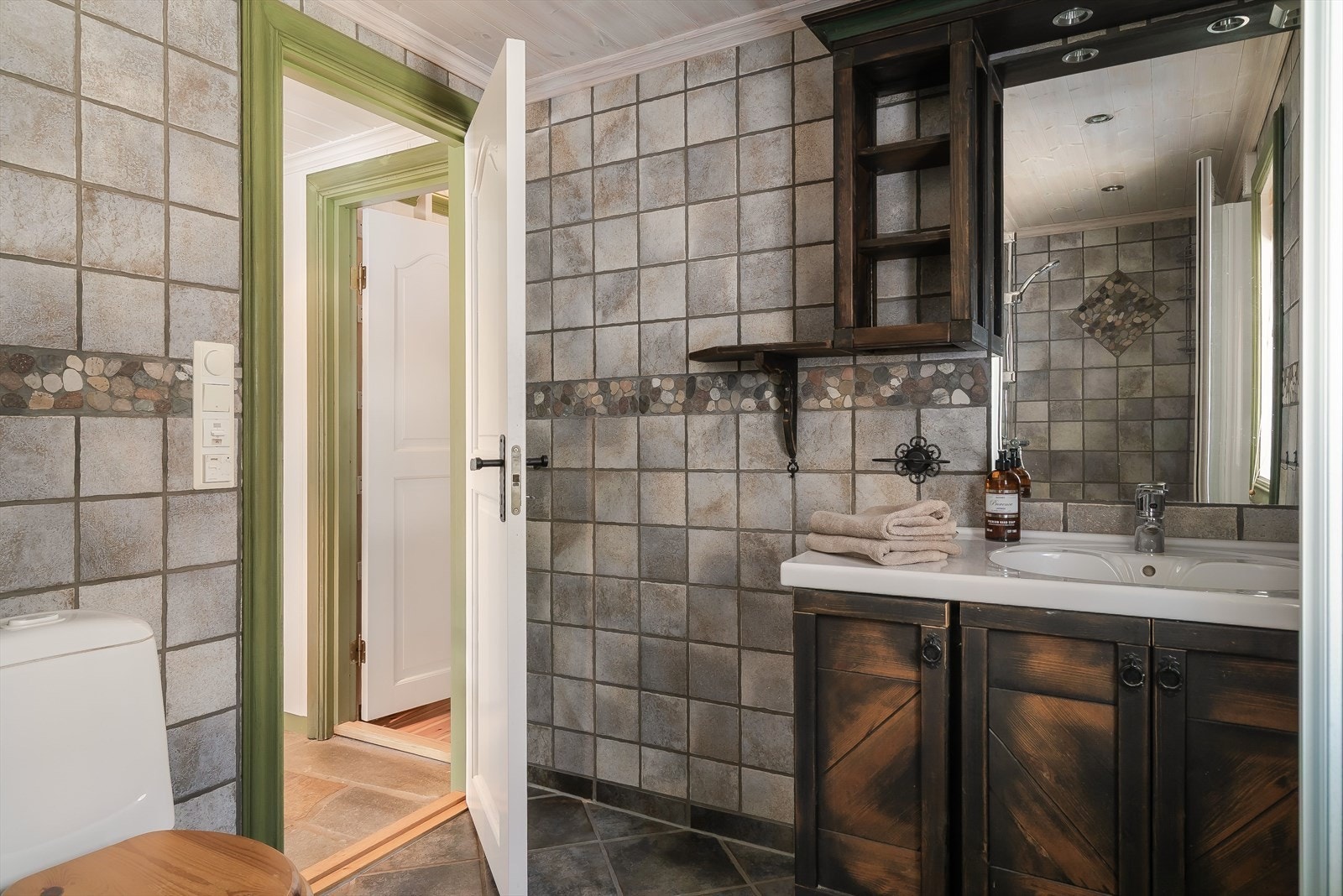 Rustikt og sjarmerende bad med flisdetalj, mørkt treverk og servant. Galleribilde