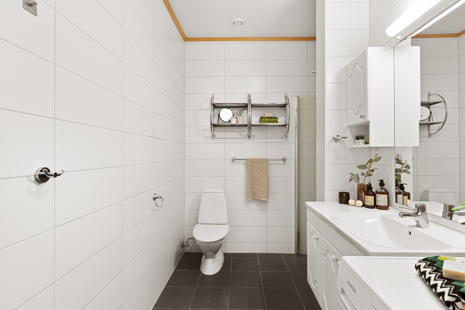 Flislagt bad i tidløs utførelse. Utstyrt med dusj, toalett og vask i seksjon. Det er også opplegg for vaskemaskin og tørketrommel. Galleribilde