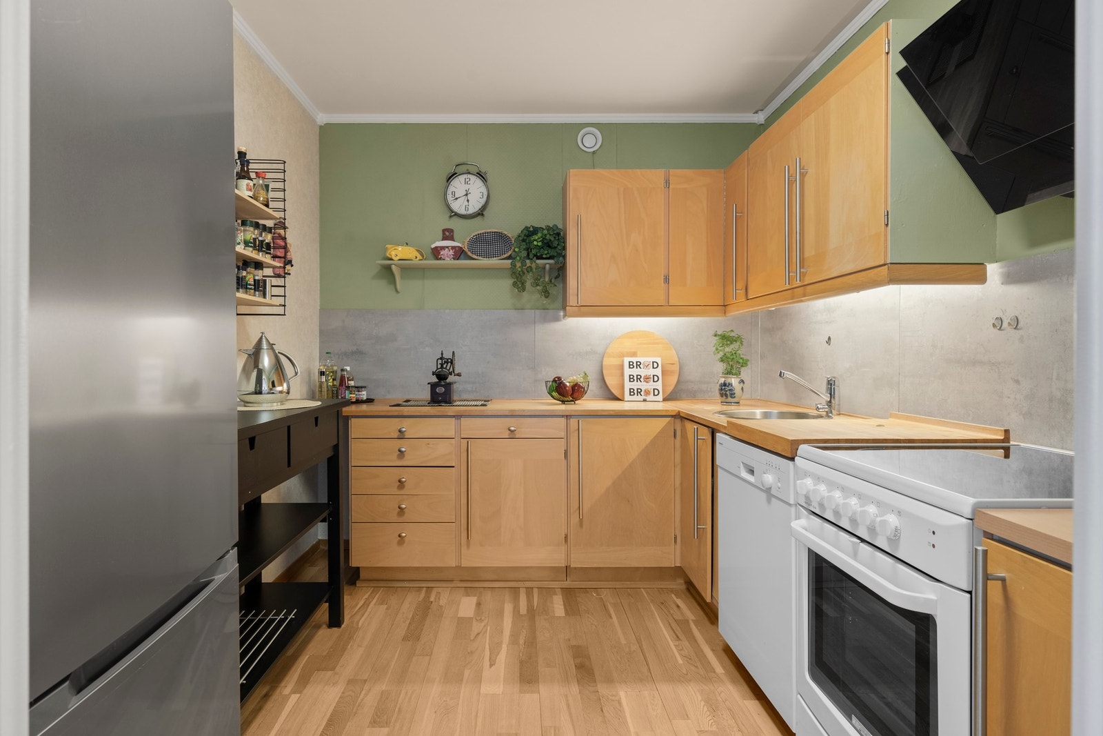 Pent kjøkken som er innredet med slette fronter, benkeplate i tre og frittstående hvitevarer Galleribilde