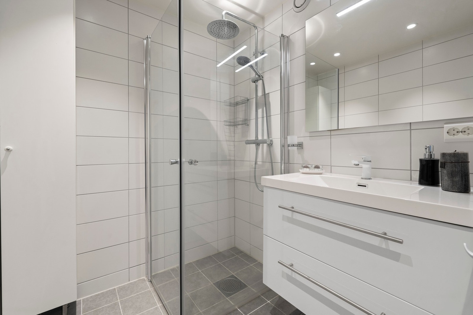 Badet er innredet med dusjhjørne med regnfallsdusj og innfellbare glassvegger, samt høyskap og servantskap og speil Galleribilde