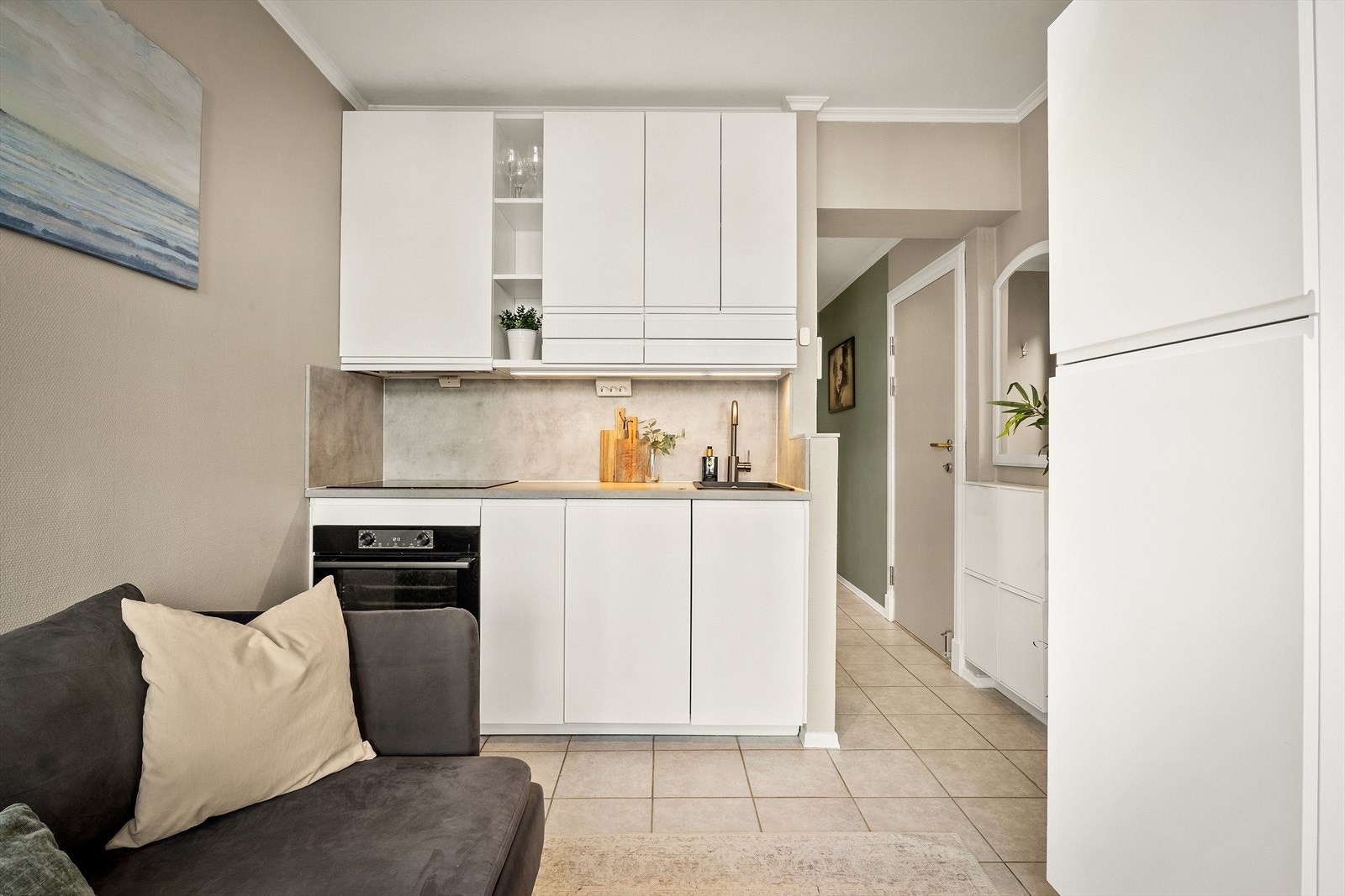 Kjøkkenet ble oppgradert i 2025 og har hvite, glatte fronter med laminat benkeplate, nedfelt vask, platetopp og kjøleskap med frysedel. Galleribilde