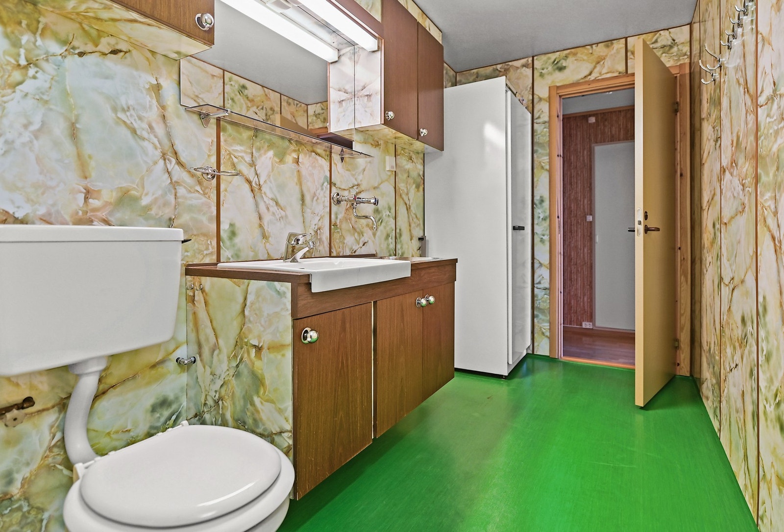 Badet er innredet med dusj, gulvstående wc, servantskap med porselensvask og stålvask, speil samt tørkeskap. Galleribilde