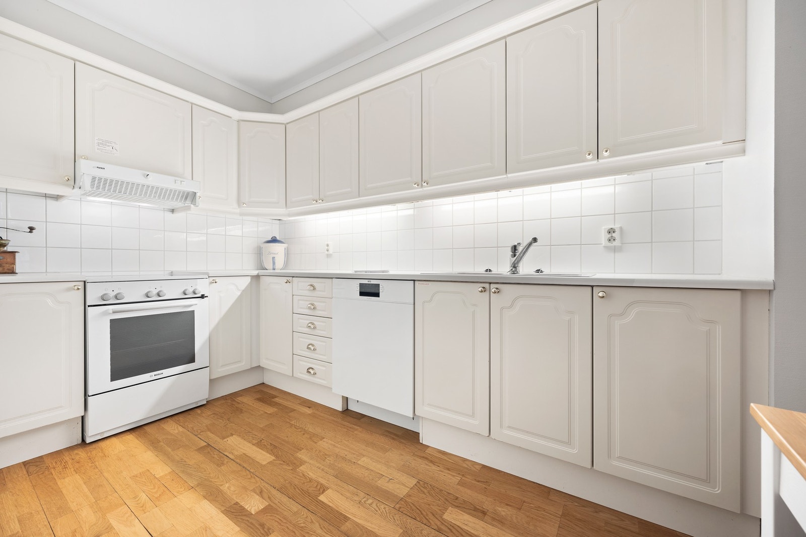 Eldre, hvit kjøkkeninnredning med profilerte fronter og laminat benkeplate. Galleribilde