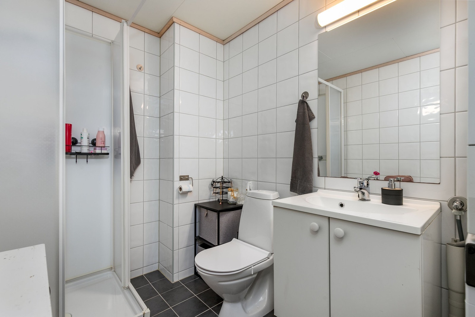 Baderomsinnredning bestående av benkeskap med glatte fronter og håndtak. Speil og belysning. Galleribilde