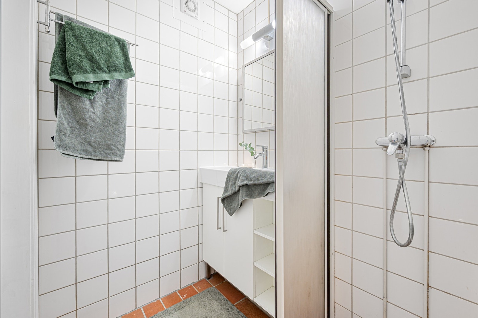 Flislagt bad med dusj, servantinnredning og praktisk oppbevaringsplass. Galleribilde