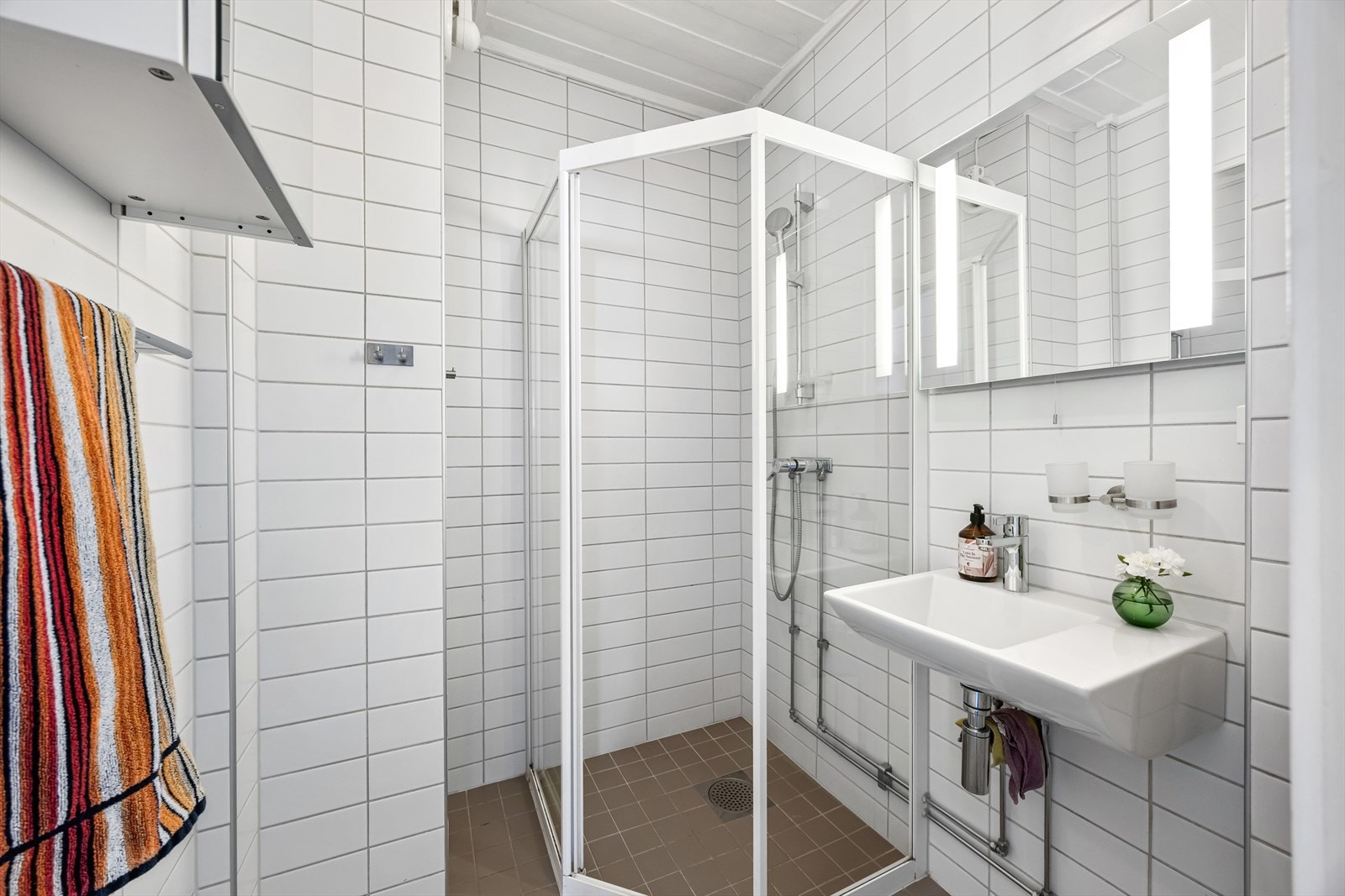 Baderommet fra 2006 har flislagte overflater, varme i gulv og en enkel servant i tillegg til skap på veggen Galleribilde