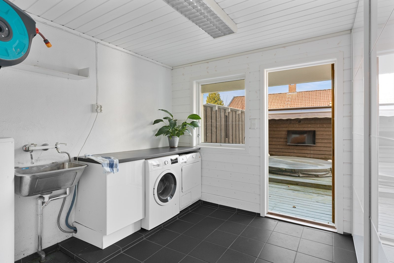 Praktisk vaskerom med fliser på gulv og utgang. Innredning med arbeidsbenk og plass til hvitevarer. Utslagsvask og skyvedørsgarderobe. Galleribilde