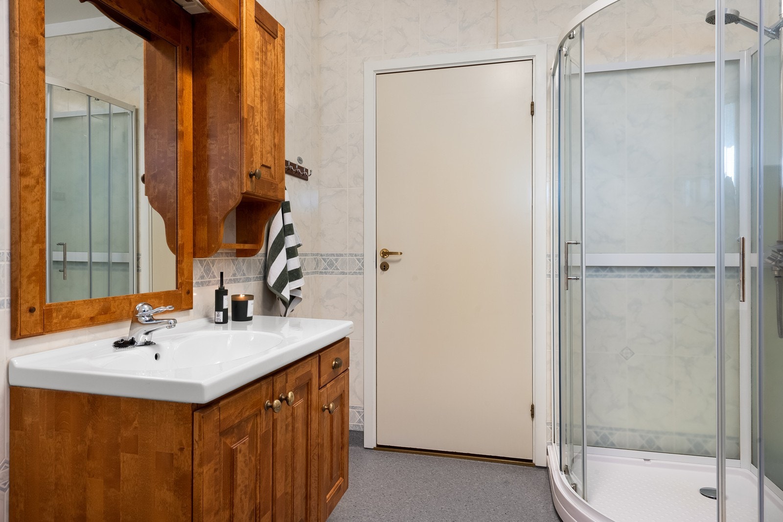 Rommet har baderomsinnredning med profilerte fronter, overhengende speil og tilhørende sideskap. Galleribilde