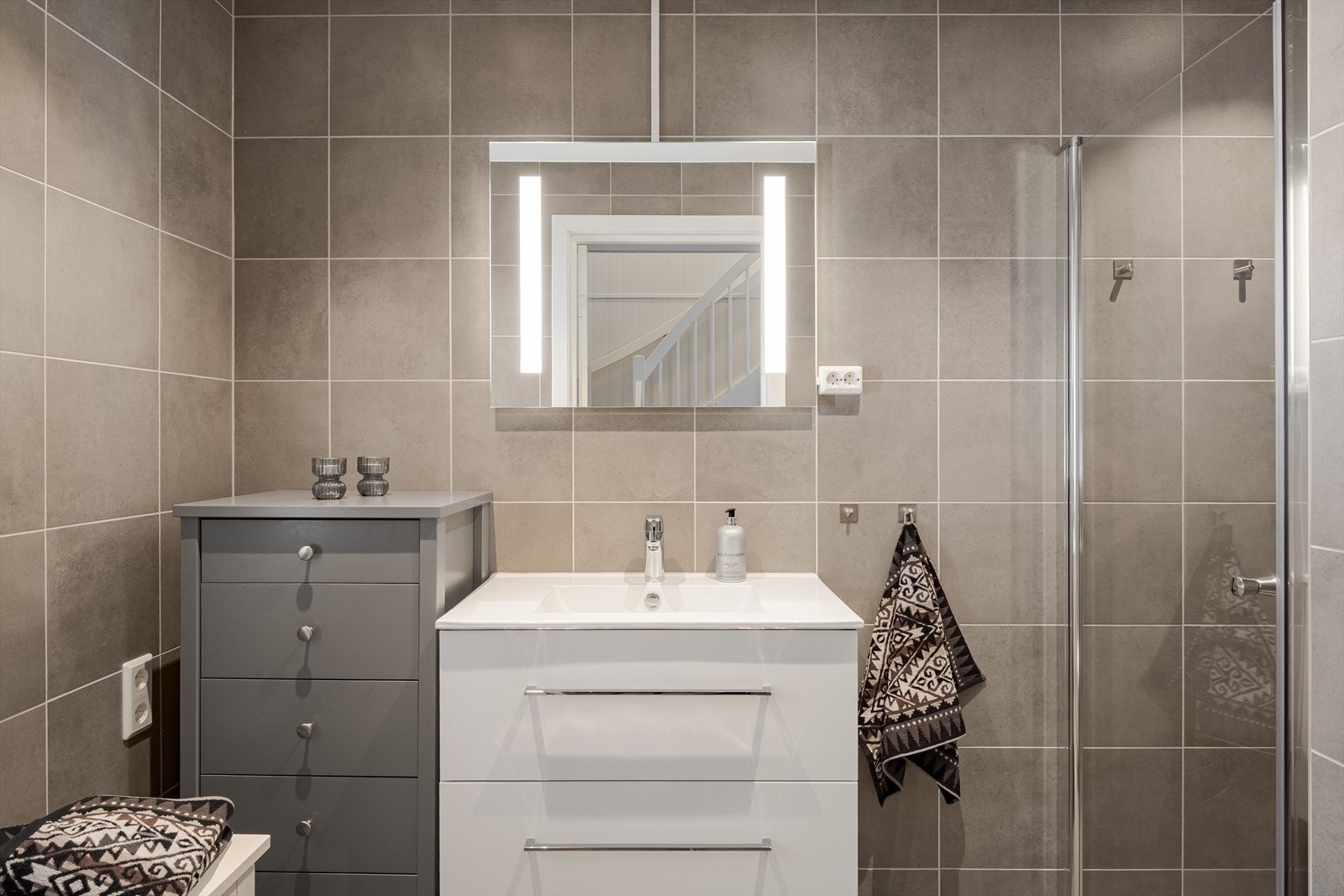 Moderne baderomsinnredning med skuffer og heldekkende servant, speil med integrert belysning over. Galleribilde