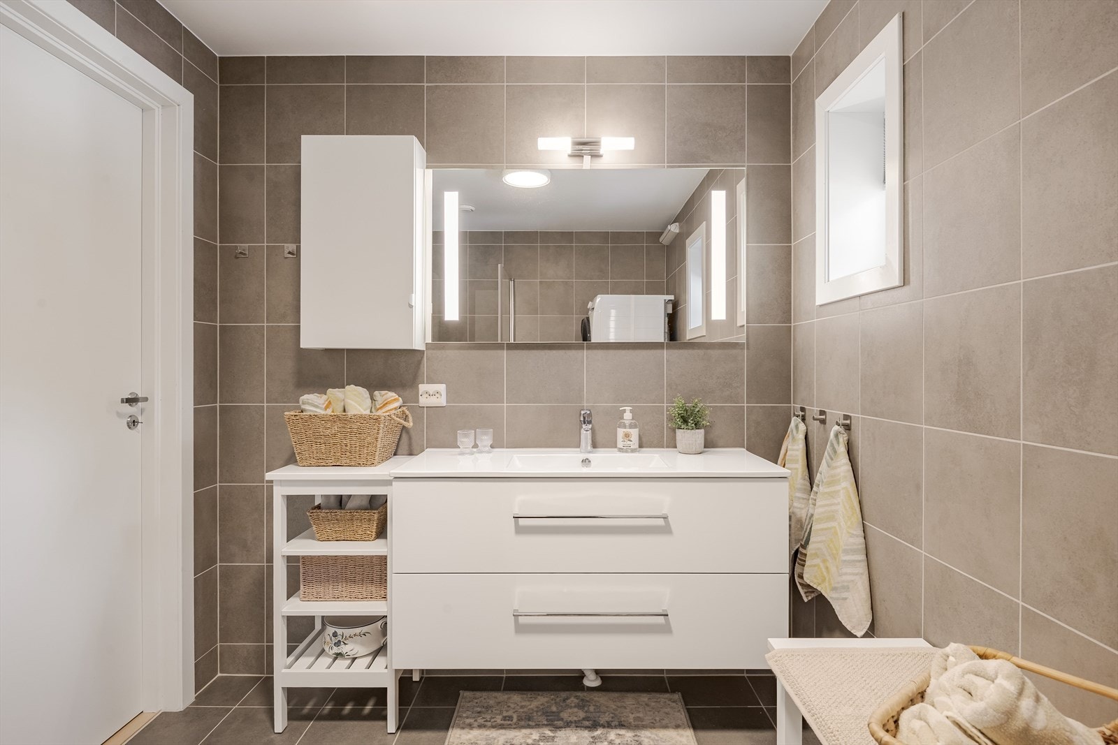 moderne baderomsinnredning med store skuffer og heldekkende servant, speil med integrert belysning og vegghengt skap over. Galleribilde