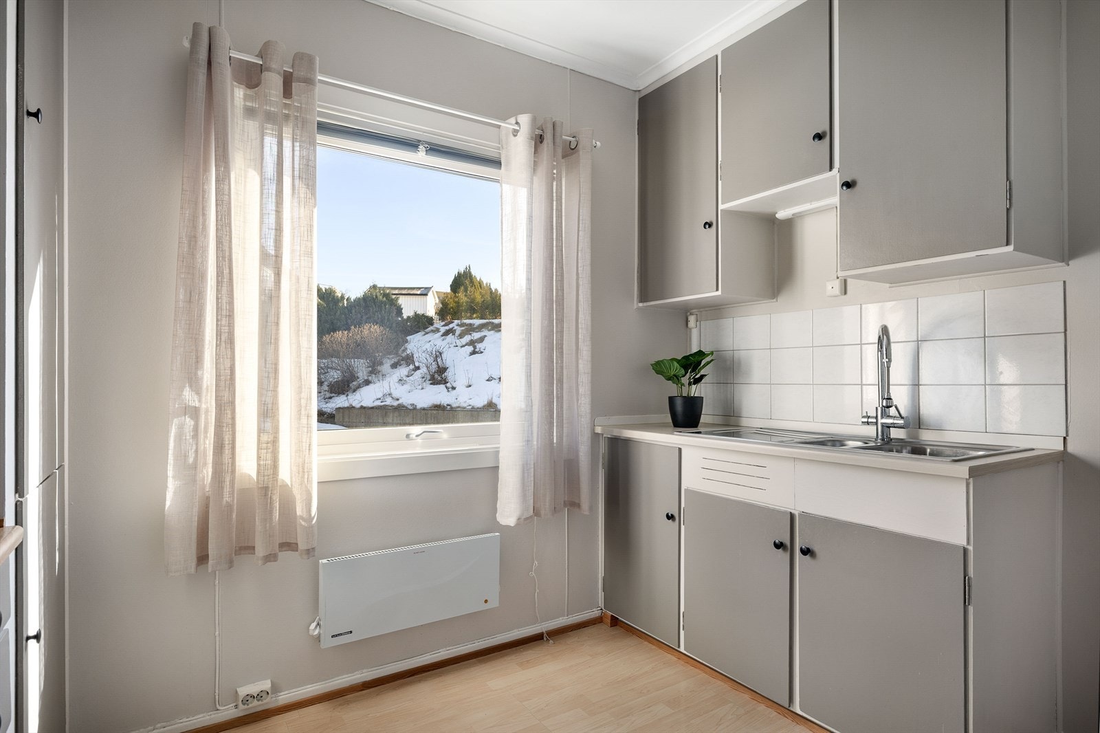 Kjøkkenet har en eldre innredning med glatte, malte skapfronter fra byggeåret, kombinert med en laminatbenkeplate med nedfelt vask. Galleribilde