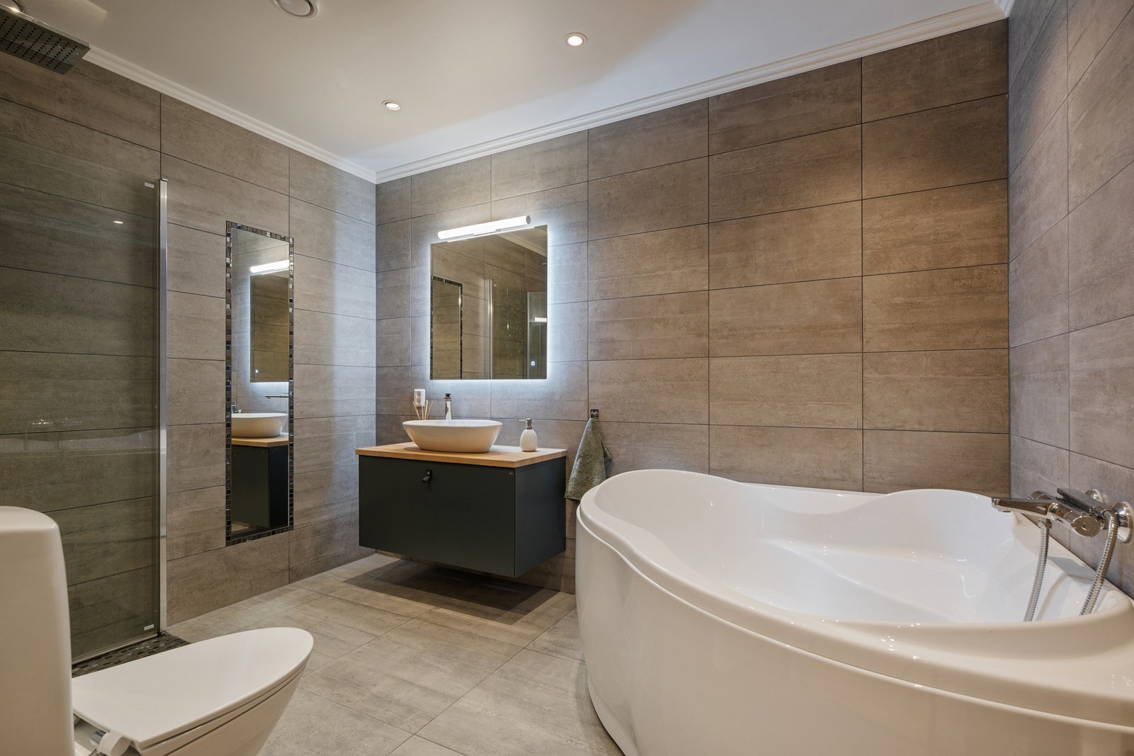 Bad med badekar, dusjhjørne, servantinnredning og toalett. Galleribilde