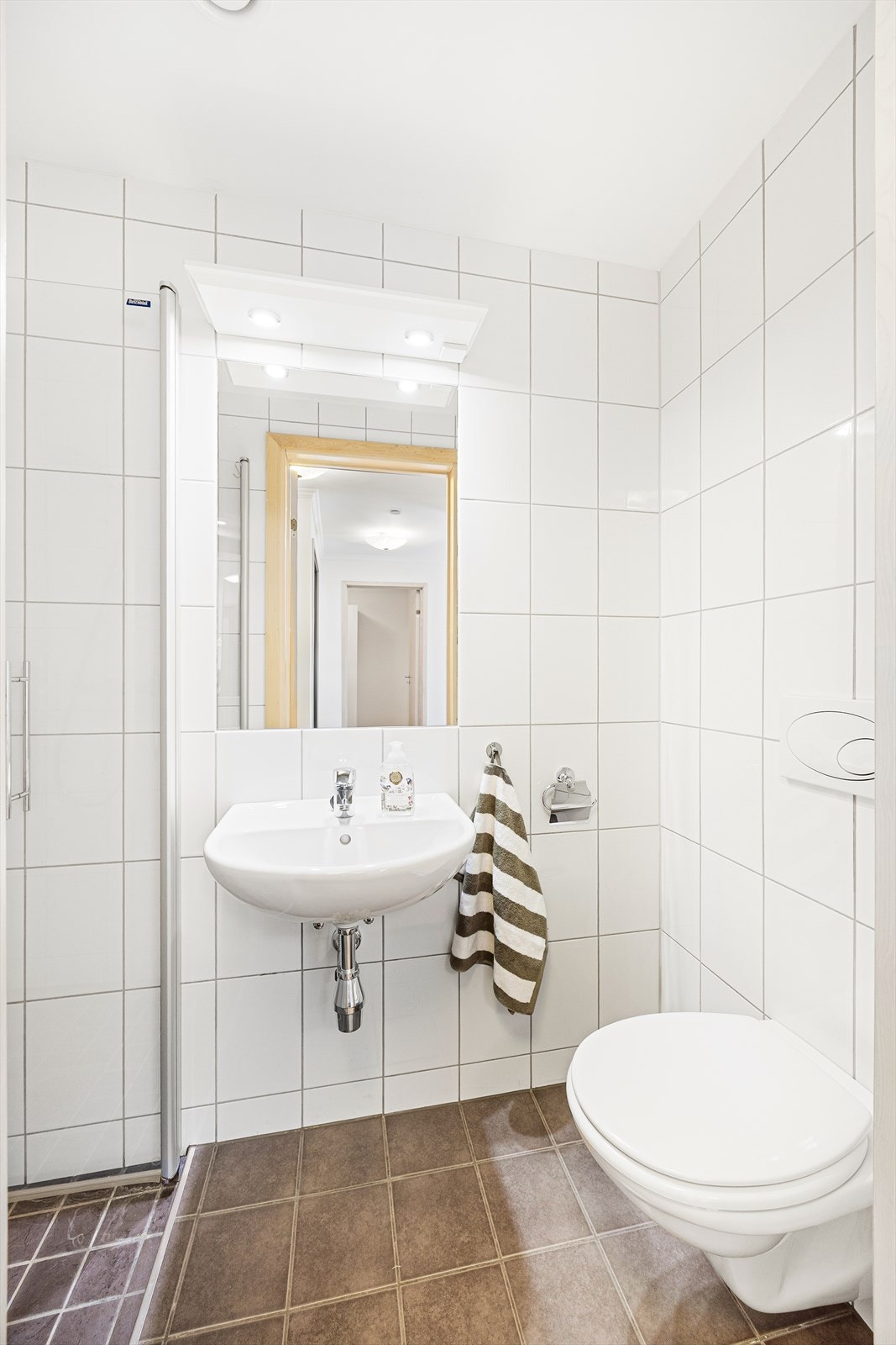 Leiligheten har også et mindre bad, som er utstyrt med vannbåren gulvvarme, veggmontert toalett og servant, samt dusjnisje. Galleribilde