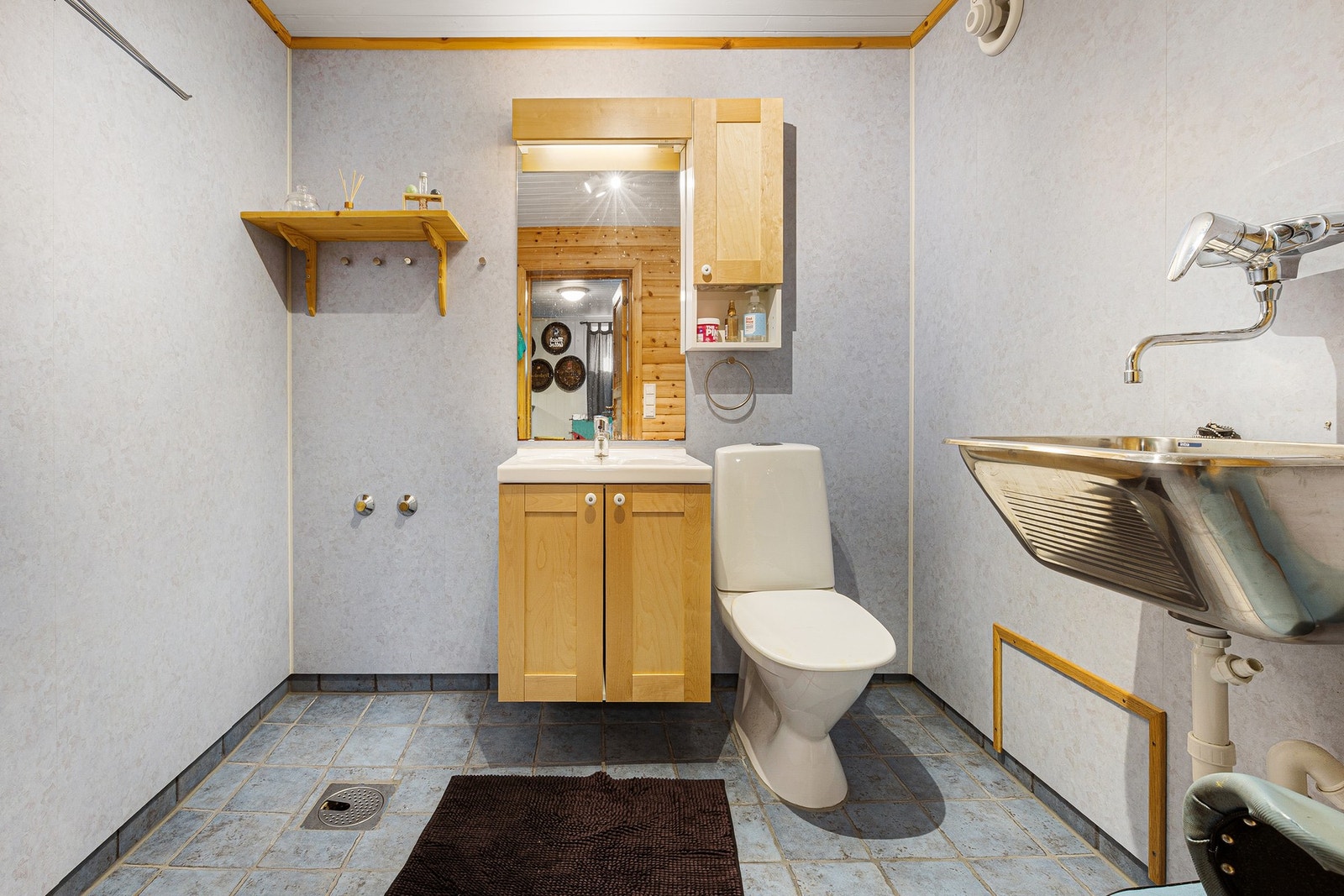 Bad har flislagt gulv og vegger med våtromsplater. Bad har gulvmontert toalett, servant i liten innredning og skyllekar montert på vegg. Galleribilde