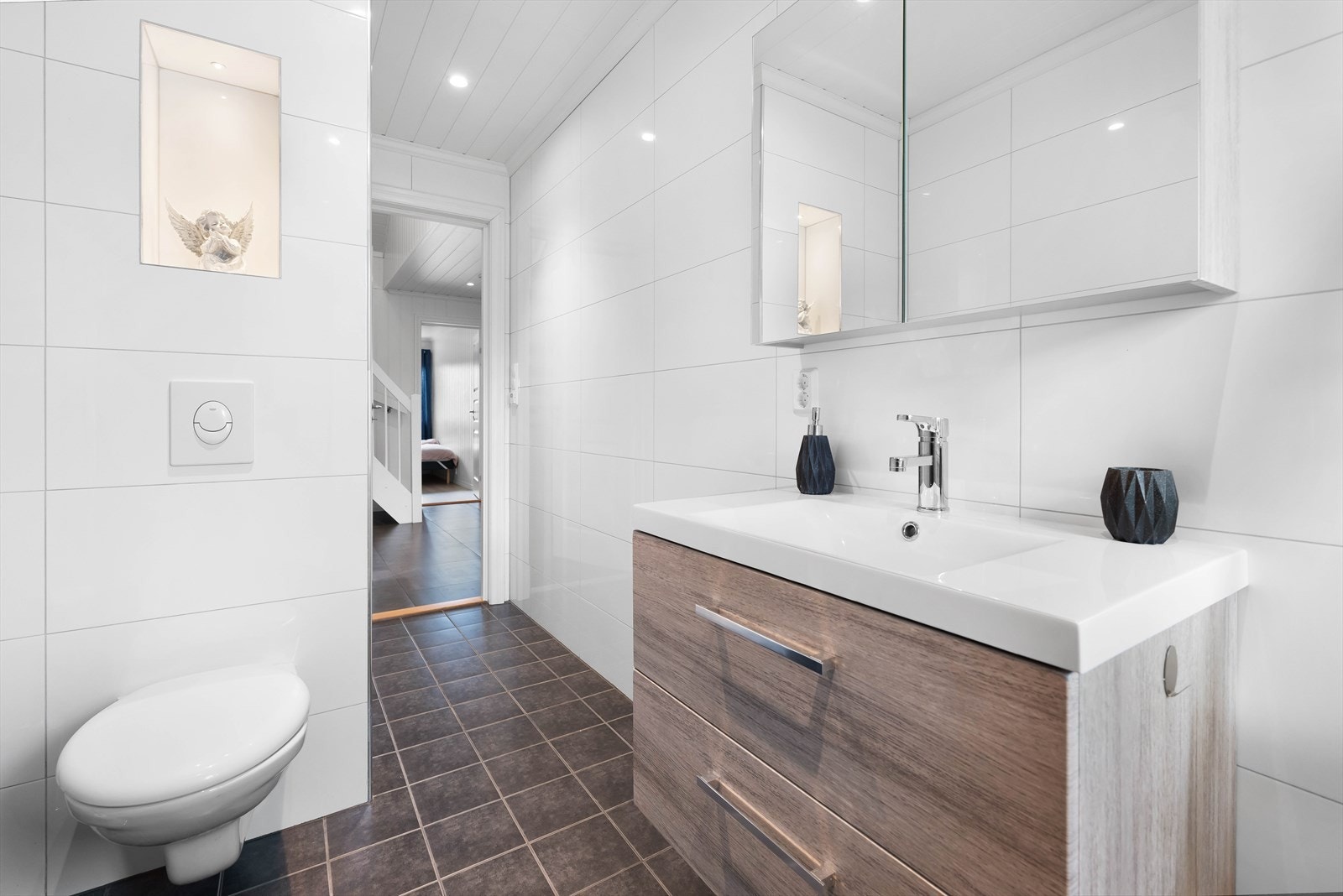 Badet er innredet med vegghengt toalett, dushjørne med glassdører og servant med skuffer. Galleribilde