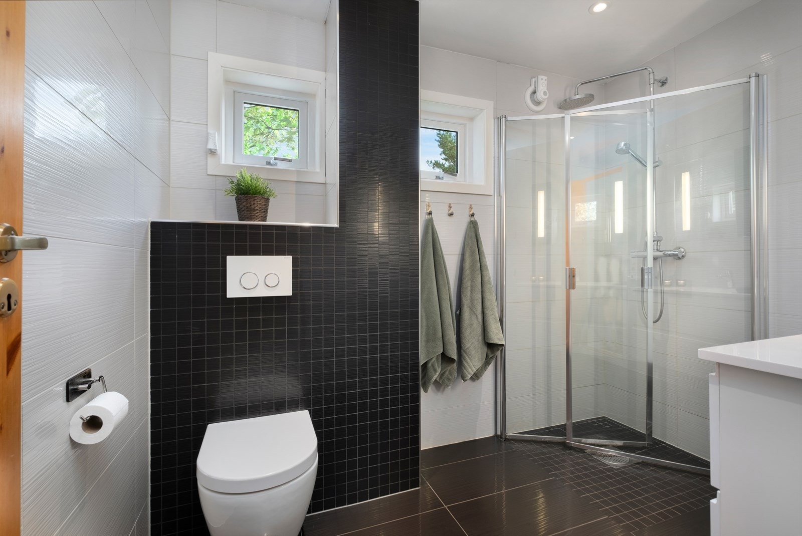 Badet byr på moderne kvaliteter som behagelig gulvvarme og mekanisk avtrekk. Det er innredet med innfellbare dusjdører av glass, dusjgarnityr på vegg, veggmontert toalett- og innredning med servant. Galleribilde