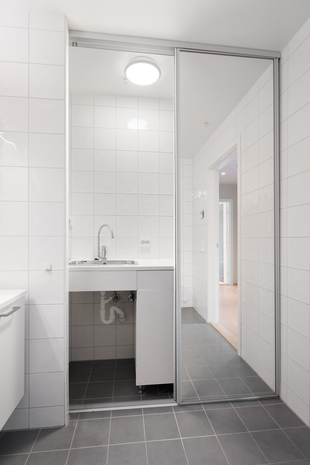 Badet har også et praktisk vaskerom skjult bak skyvedører hvor det er utslagsvask i rustfritt stål og opplegg for vaskemaskin Galleribilde