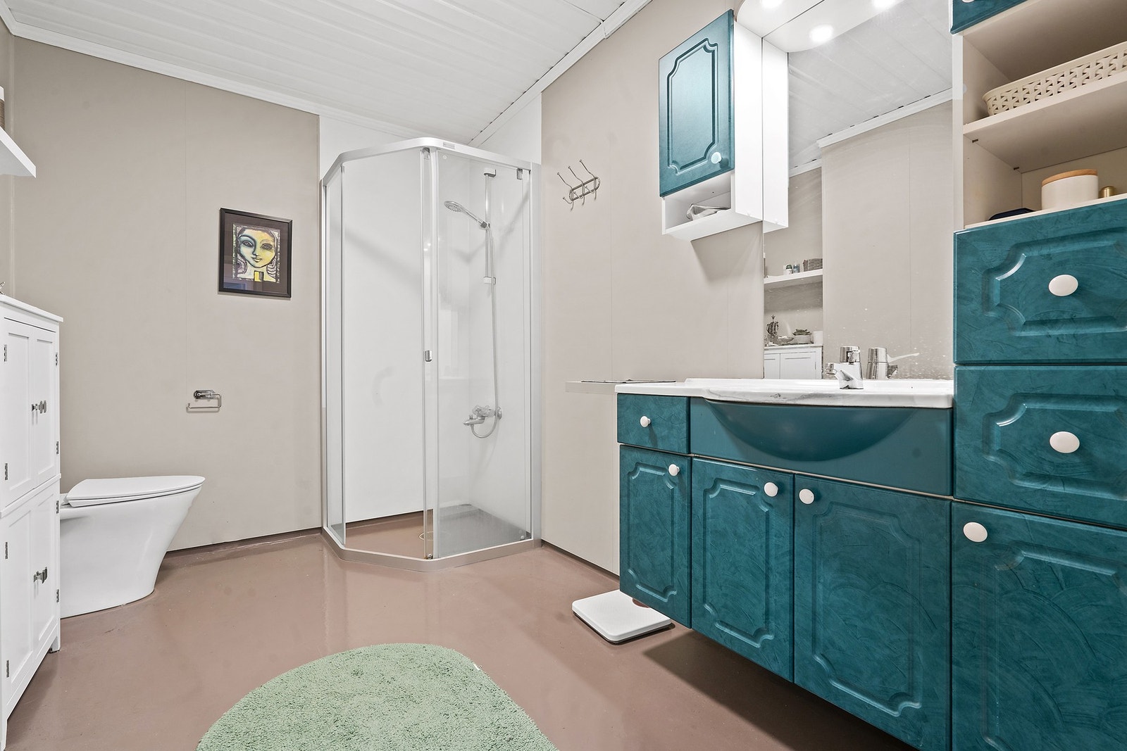 Badet er utstyrt med dusjhjørne, toalett og innredning med servant. Gulvet har vinylbelegg. Galleribilde