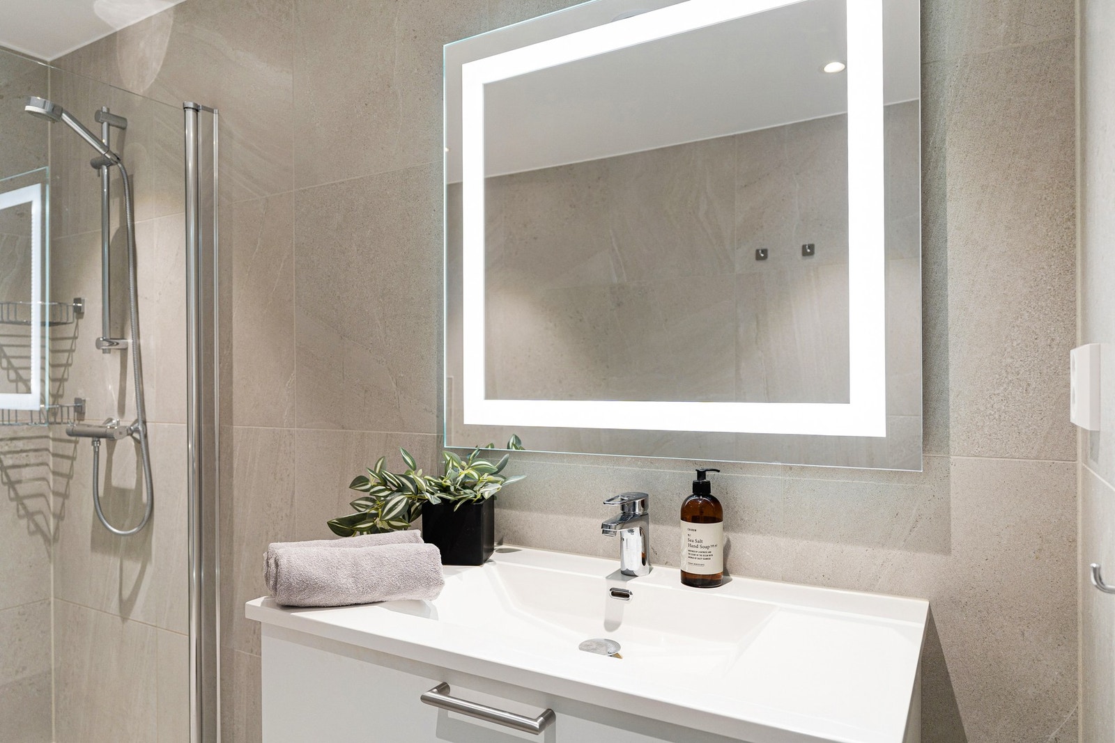 Baderomsinnredning med servant og underskap med god plass til hygieneartikler samt speil med innebygd belysning. Galleribilde