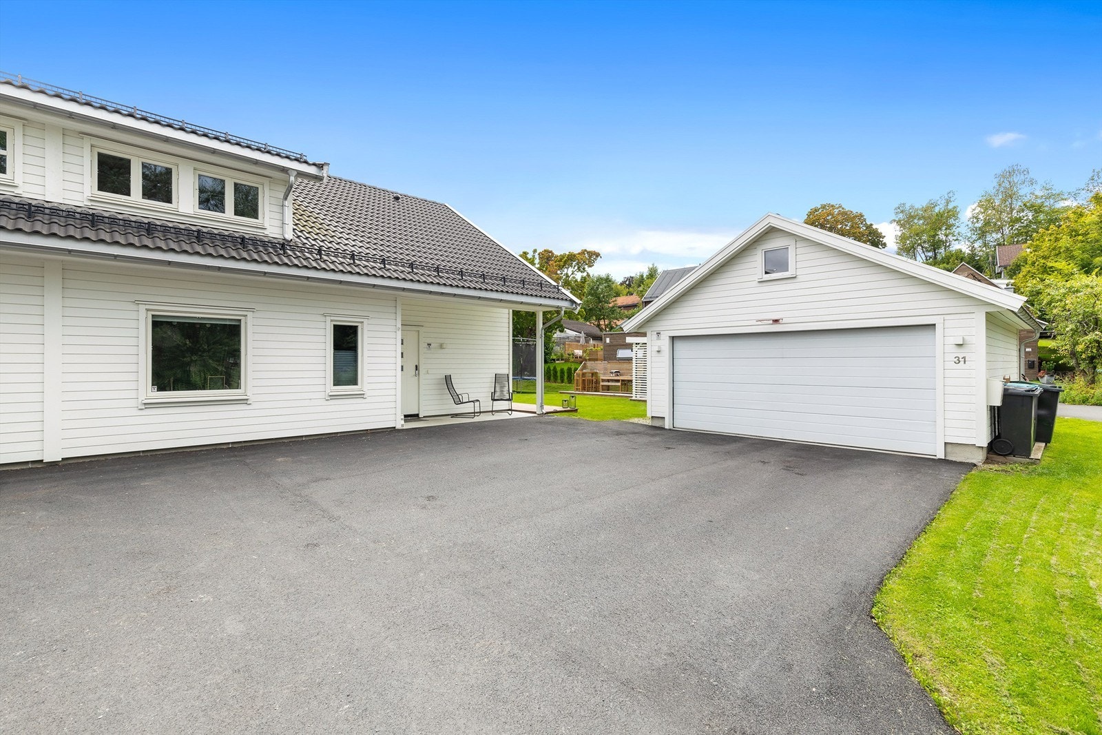 Asfaltert gårdsplass og frittstående garasje med lader for elbil. Galleribilde