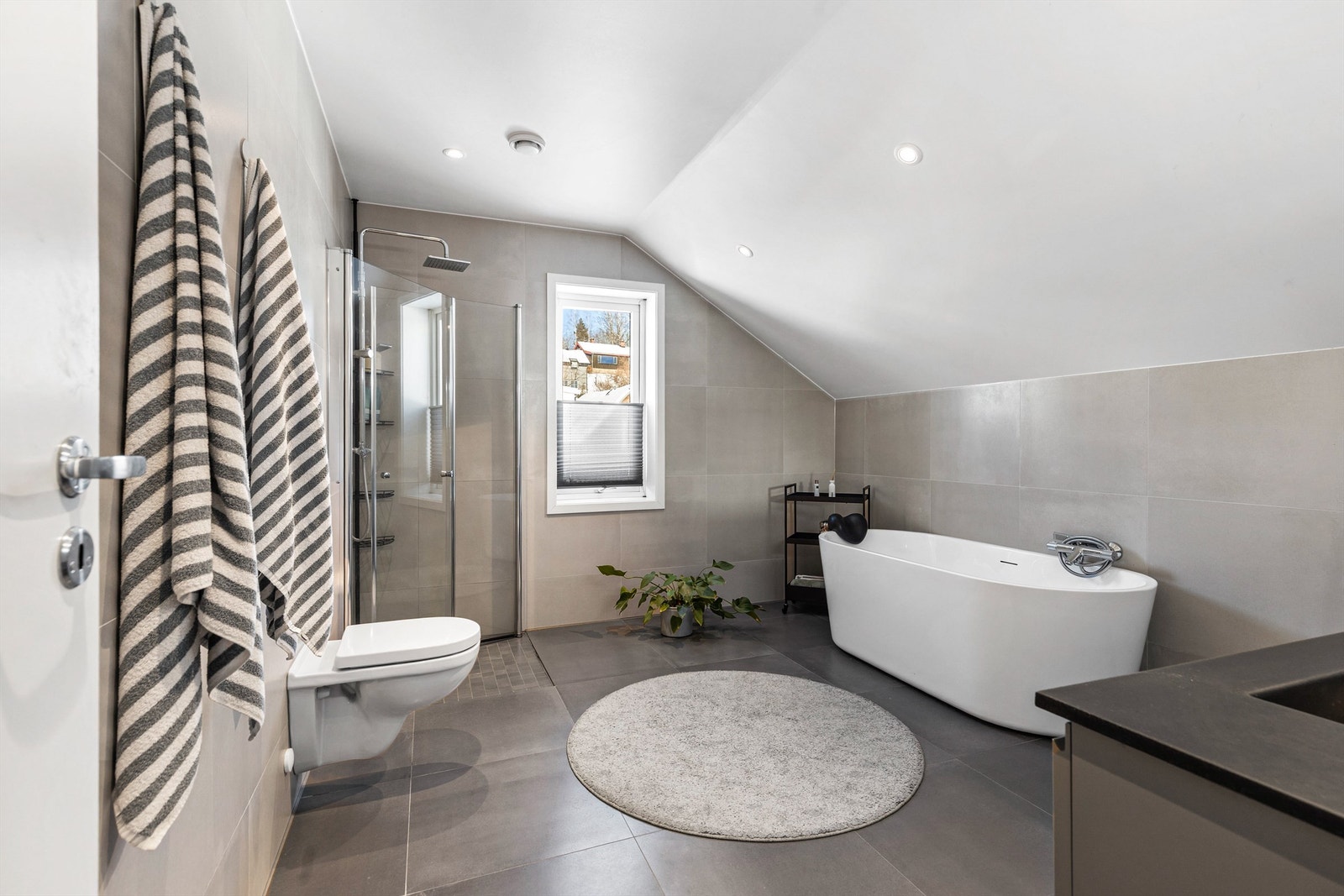 Badet i loftsetasjen har flislagt gulv med gulvvarme. Nedsenket himling med downlights. Vegghengt servantinnredning. Dobbel ovenpåliggende servant med armaturer. Galleribilde