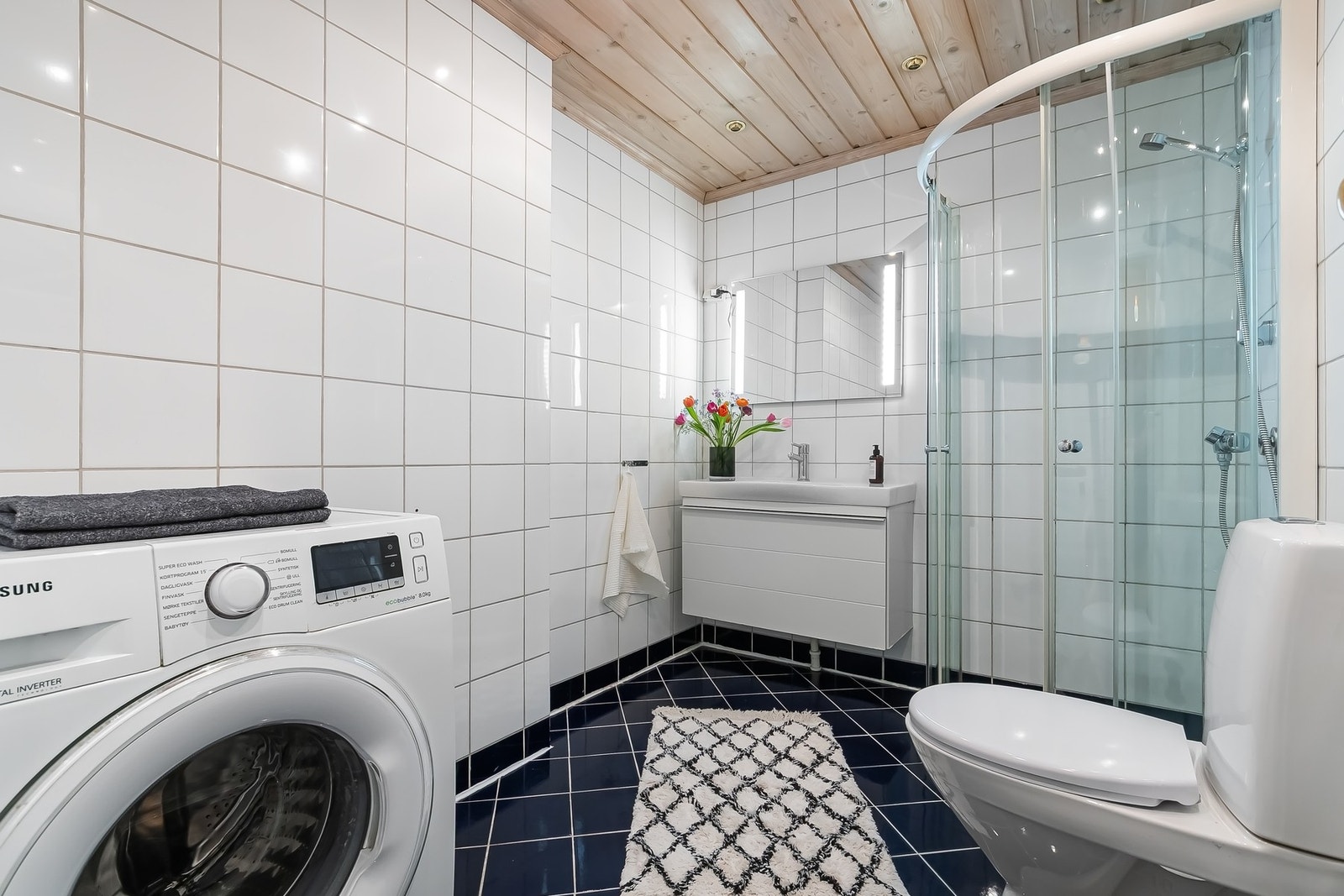 Lyst og helfliset baderom med trepanel i himlingen og downlights Galleribilde