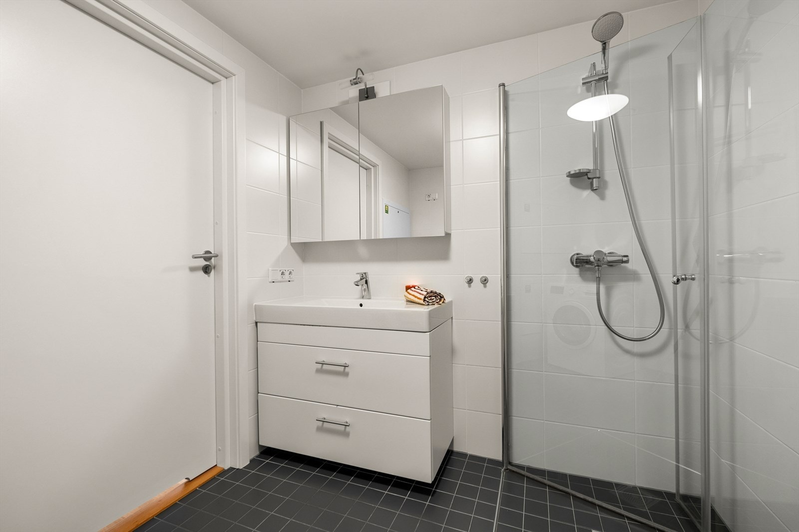 Pent og lyst flislagt bad på 5,5 m² utstyrt med vegghengt toalett, dusjhjørne og opplegg for vaskemaskin. Galleribilde